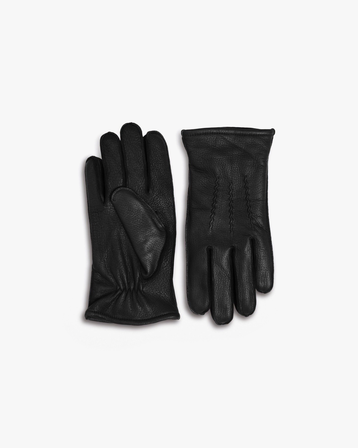 A pair of black deer leather gloves with a subtle grain texture, gentle gathers at the wrist, and fine stitching detail, displayed flat on a white background to highlight their refined Scandinavian design.