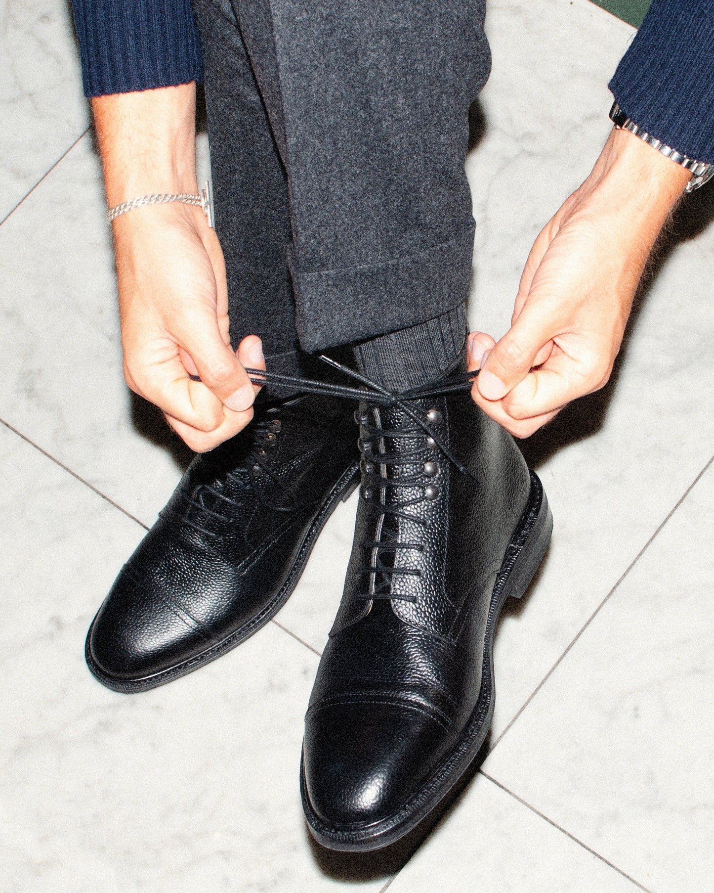 Abisko in black country calf being laced up, highlighting the grained leather upper, cap toe, and sturdy lace-up design, paired with dark wool trousers for a polished, versatile look.