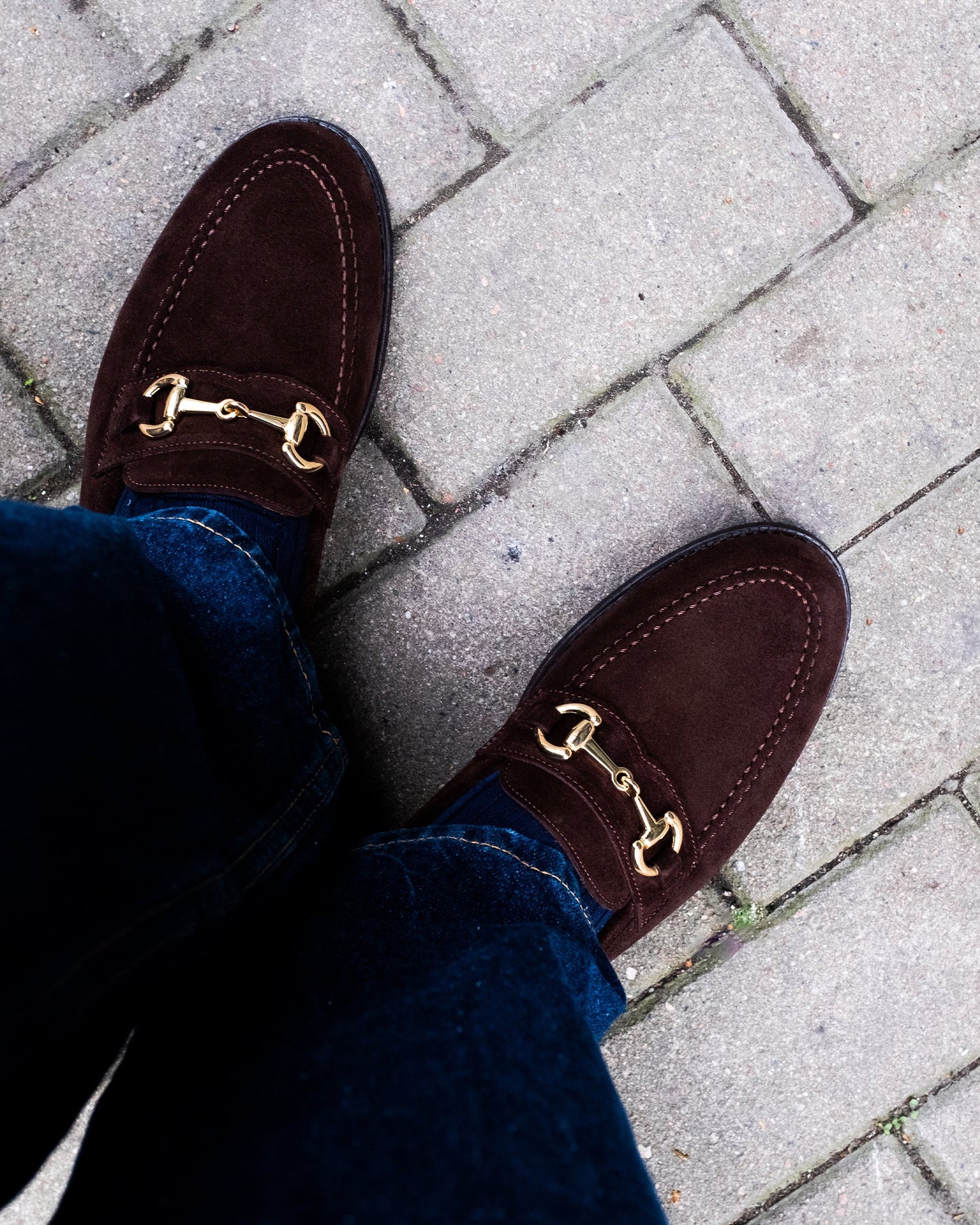 Karlberg in dark brown suede worn with denim, highlighting the gold-toned horsebit detail and fine stitching, styled for a casual outdoor setting.