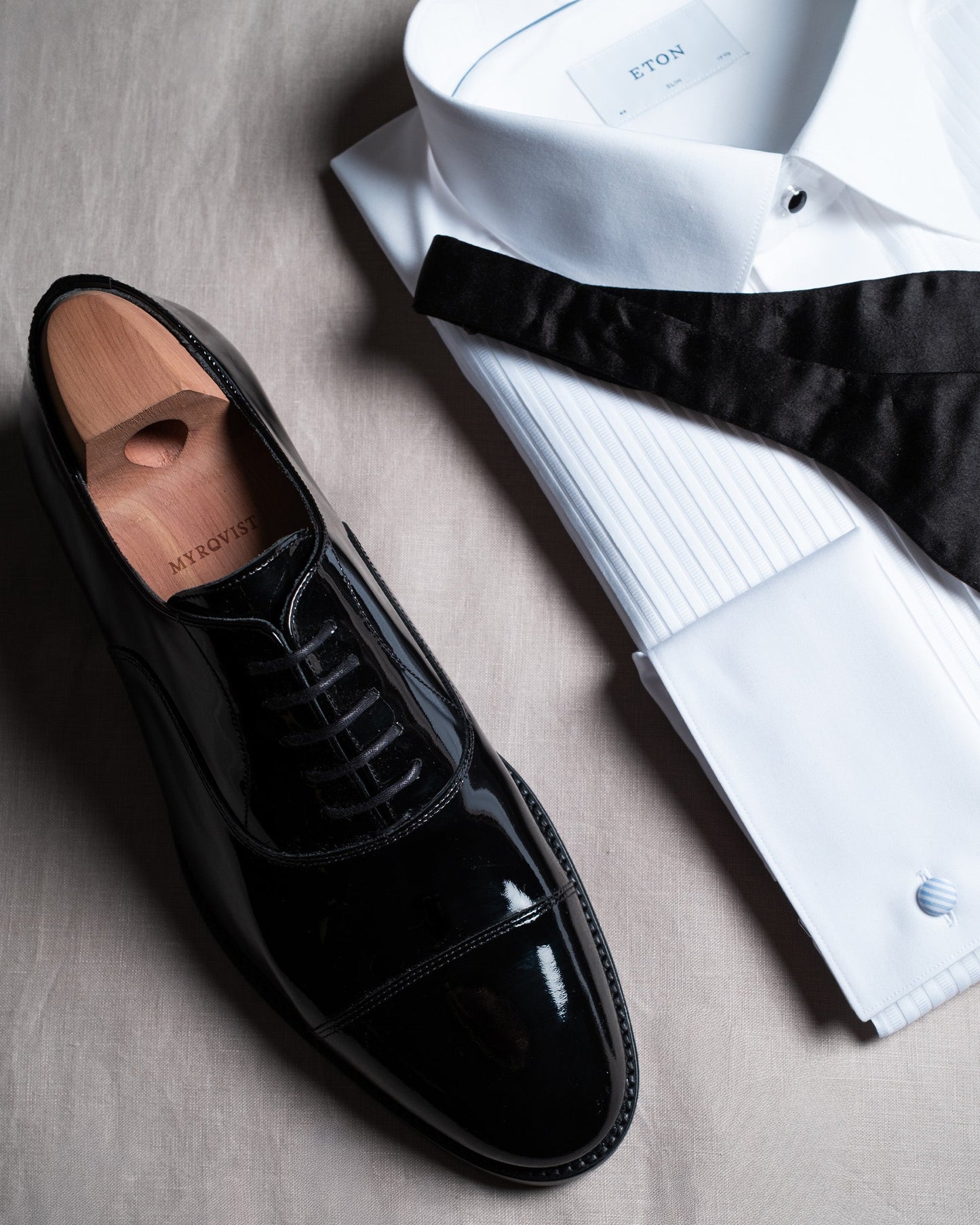 Vinterviken II in black patent leather shown with a crisp white tuxedo shirt and black bow tie, highlighting the shoe's glossy finish and formal styling for black tie events.