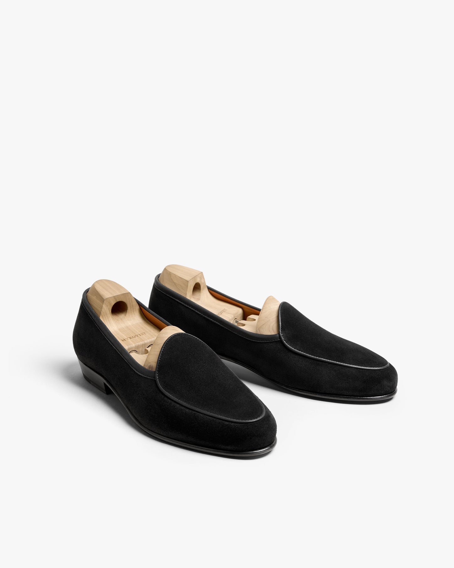Ängby in black suede displayed at an angle, featuring a soft suede finish, clean piping, and wooden shoe trees that preserve the elegant Belgian loafer silhouette.