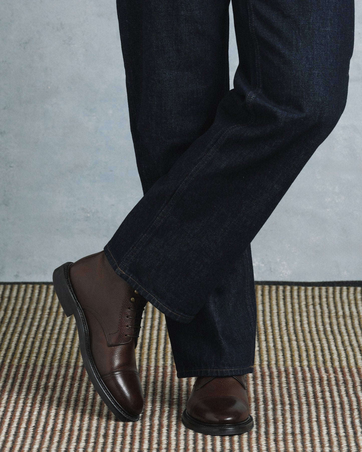 Abisko in dark brown country calf worn with dark denim, showcasing the textured grained leather, cap toe, and sturdy rubber sole for a refined yet versatile style suitable for both casual and dressed-up occasions.