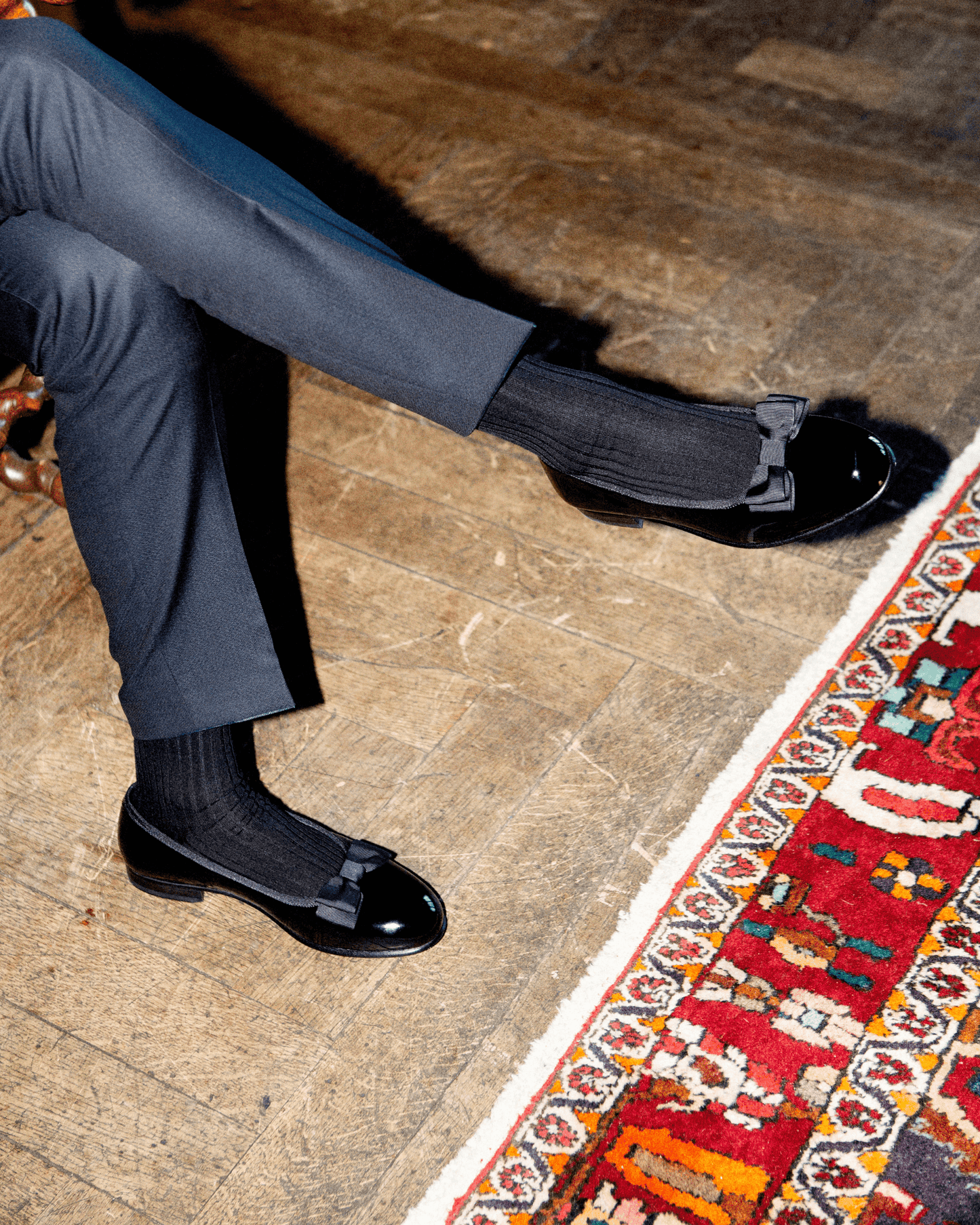 Rosendal in black patent leather styled with dark socks and tailored trousers, featuring a glossy finish and grosgrain bow, perfect for formal events or black tie occasions.