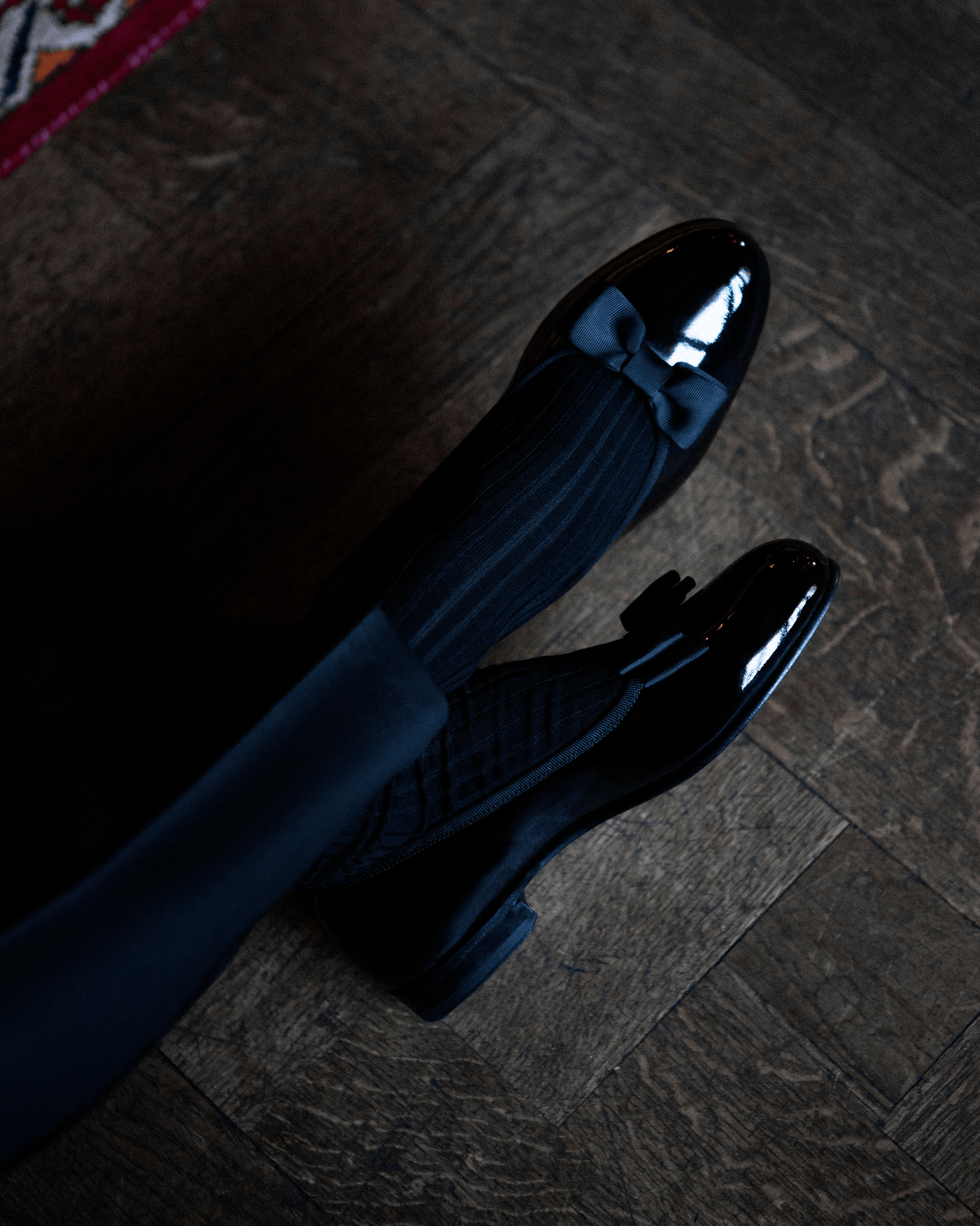 Rosendal in black patent leather worn with dark formal socks, showcasing the glossy opera pump silhouette and grosgrain bow detail, ideal for pairing with tuxedos or evening suits at elegant events.