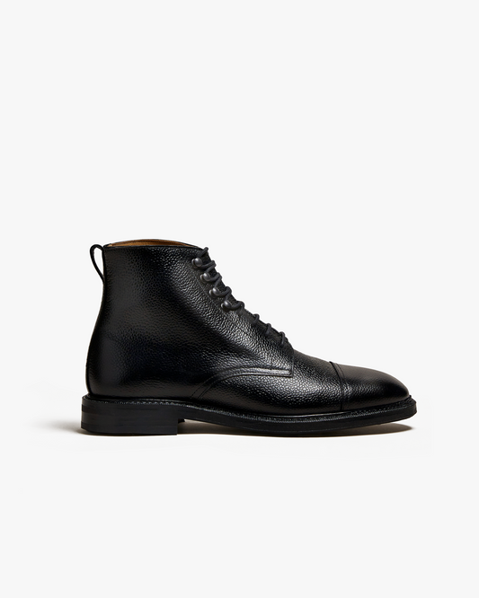 Abisko in black country calf features a grained leather upper with a cap toe, lace-up closure, and pull tab, set on a sturdy rubber sole for versatile wear with wool trousers or denim.