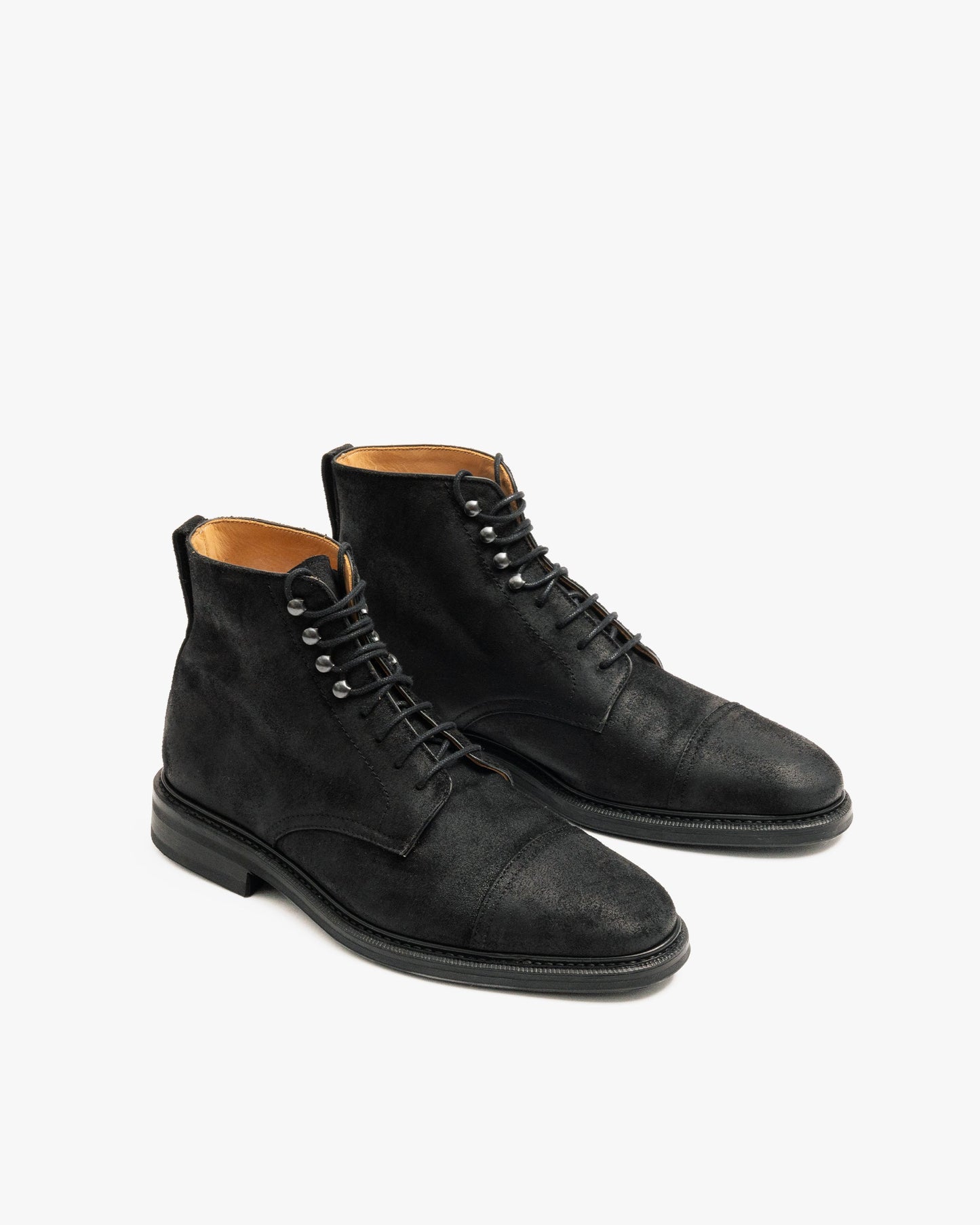 Abisko in black waxed suede features a pair of matte black cap toe boots with lace-up closure, subtle stitching, and a durable rubber sole, designed for both city wear and outdoor winter settings.