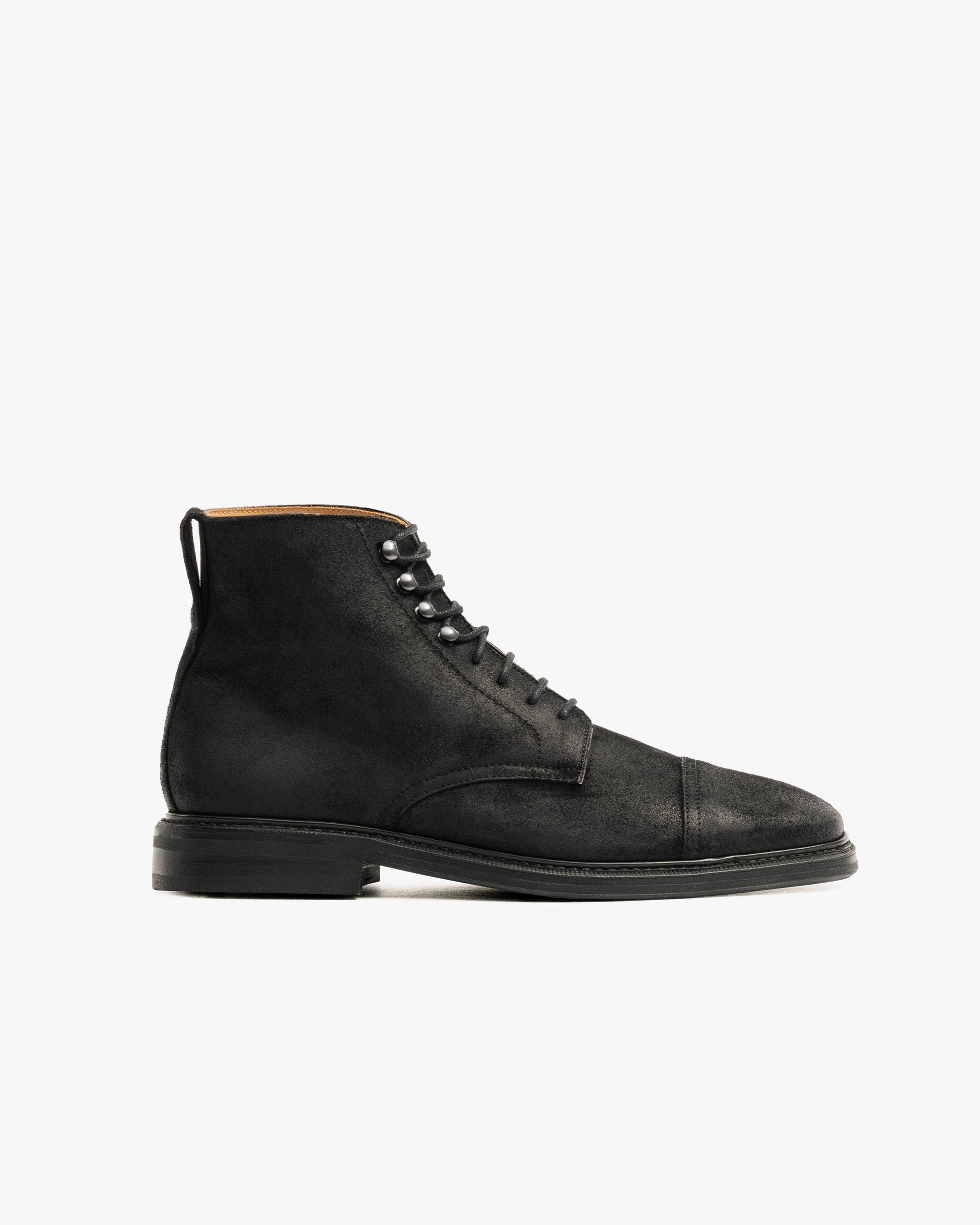 Abisko in black waxed suede features a matte black cap toe boot design with a lace-up front, subtle stitching, and a sturdy double studded rubber sole, offering a refined yet resilient look ideal for winter wear.