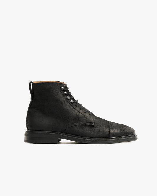 Abisko in black waxed suede features a matte black cap toe boot design with a lace-up front, subtle stitching, and a sturdy double studded rubber sole, offering a refined yet resilient look ideal for winter wear.