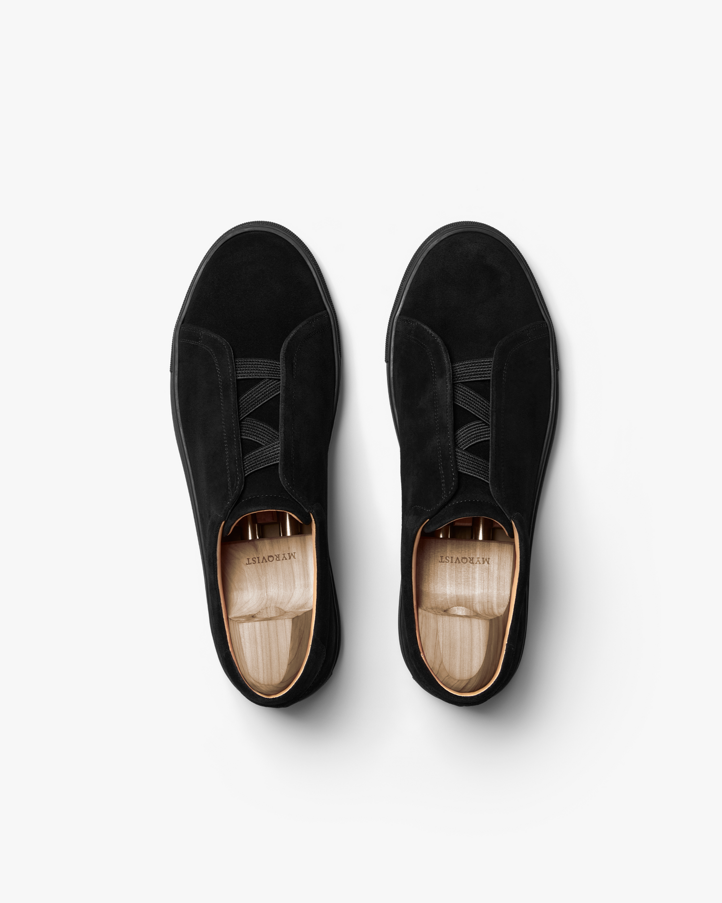 Pair of Alnö Monochrome II sneakers in black suede shown from above, highlighting the seamless uppers, elastic lacing system, and wooden shoe trees inside each shoe.