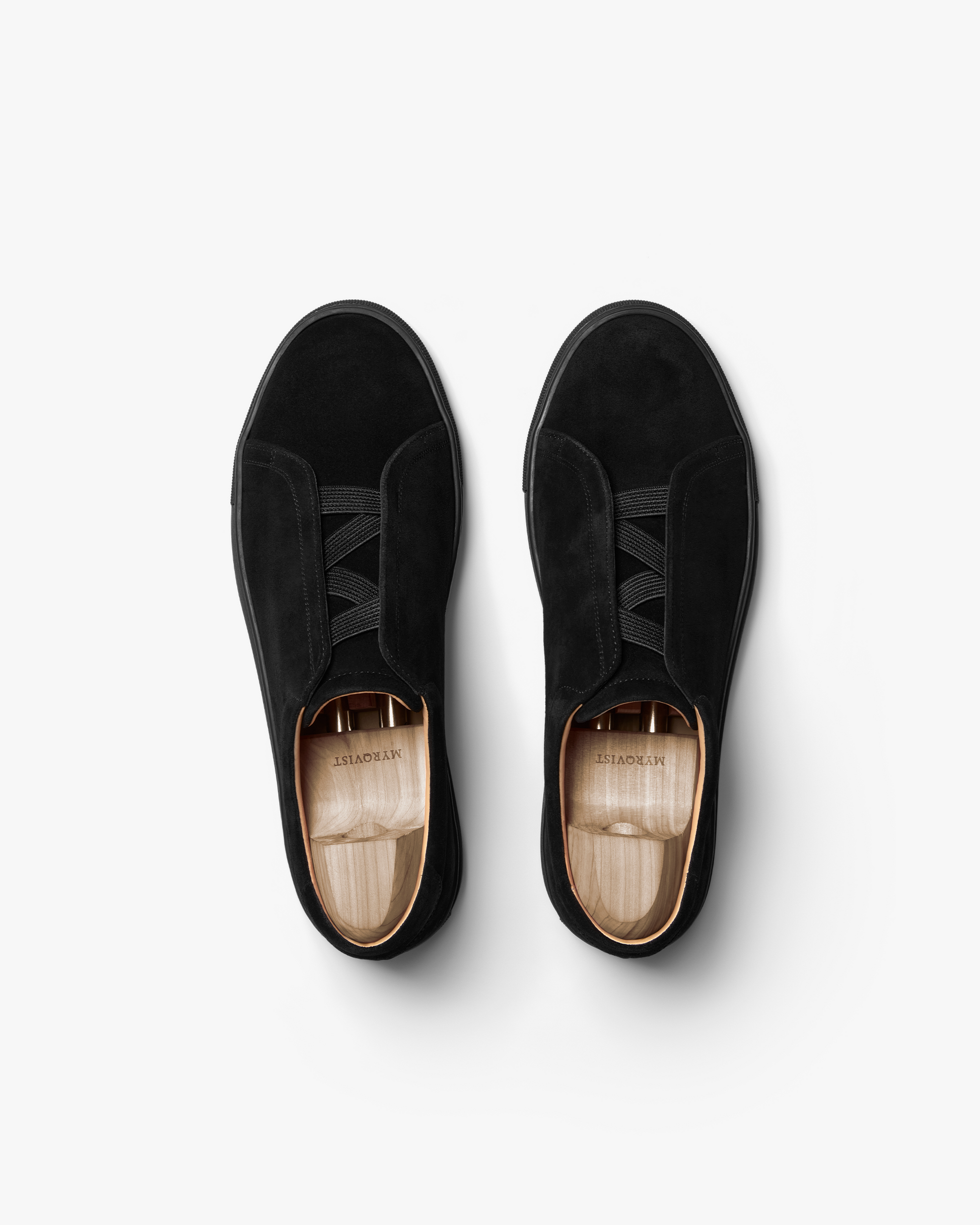 Pair of Alnö Monochrome II sneakers in black suede shown from above, highlighting the seamless uppers, elastic lacing system, and wooden shoe trees inside each shoe.