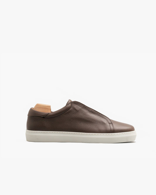 Low-top Alnö II sneaker in brown natural grain leather with a softly rounded toe, minimalist concealed lacing, and a contrasting white cup sole, shown in profile on a plain background.