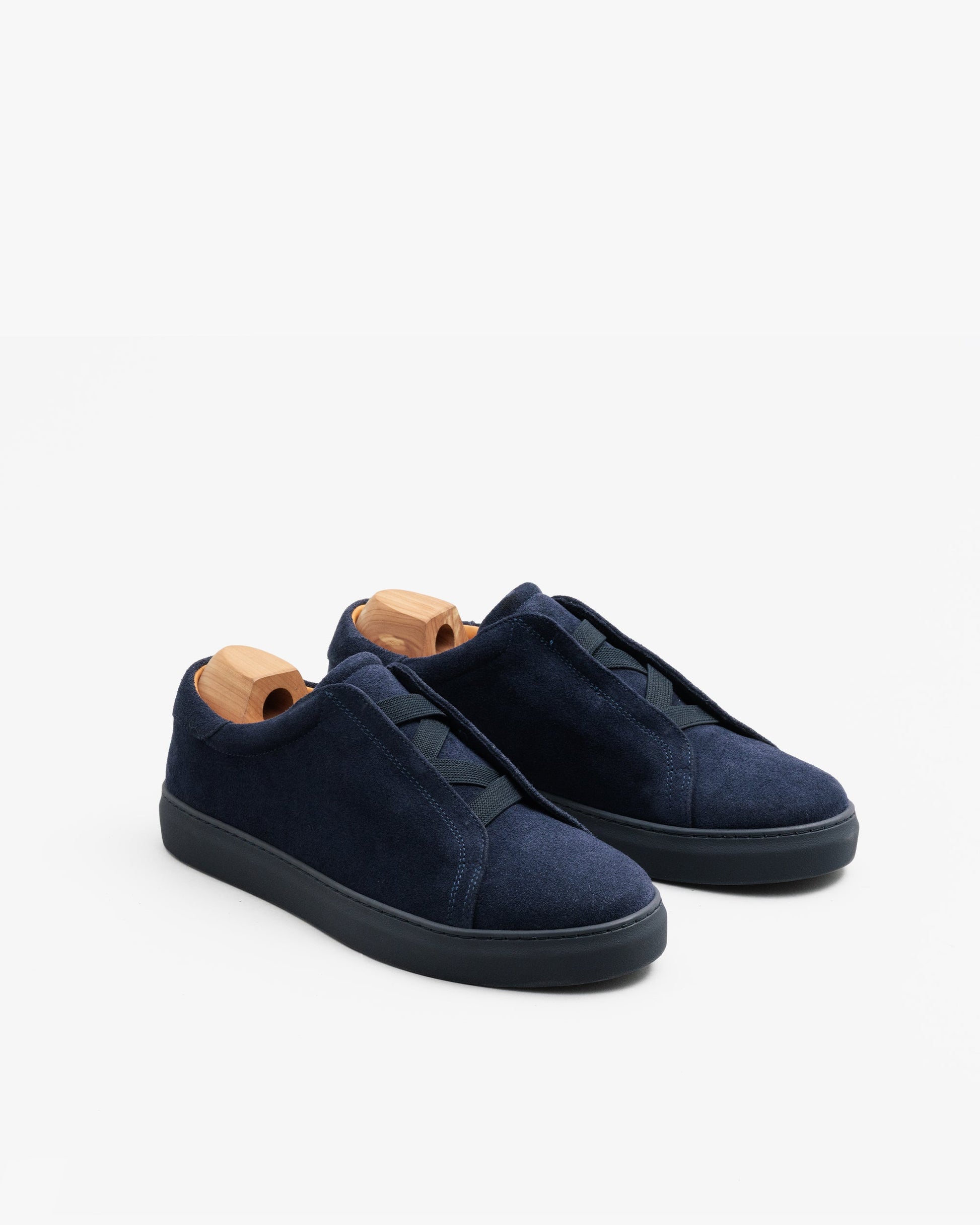 Alnö Monochrome II sneakers in midnight blue suede with a seamless, laceless design, tonal rubber soles, and wooden shoe trees inserted, shown at a three-quarter angle.
