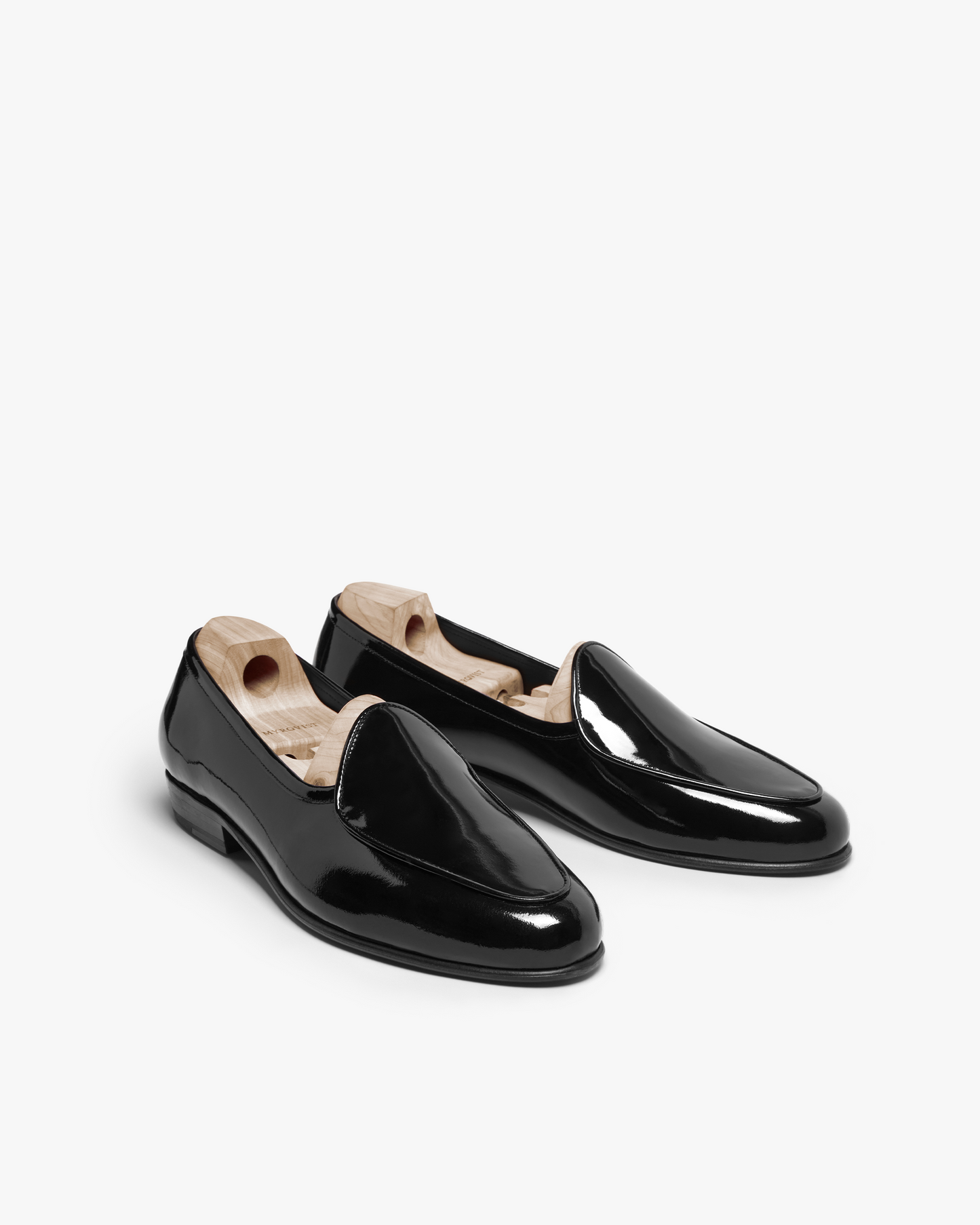 Ängby in black patent leather features a glossy, mirror-like finish with a gently rounded toe and subtle piping, shown with wooden shoe trees for maintaining shape.