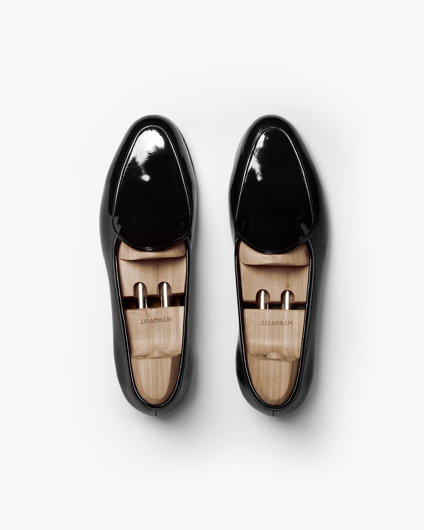 A pair of Ängby in black patent leather shown from above, highlighting the glossy finish, gently rounded toe, and wooden shoe trees inside each loafer.