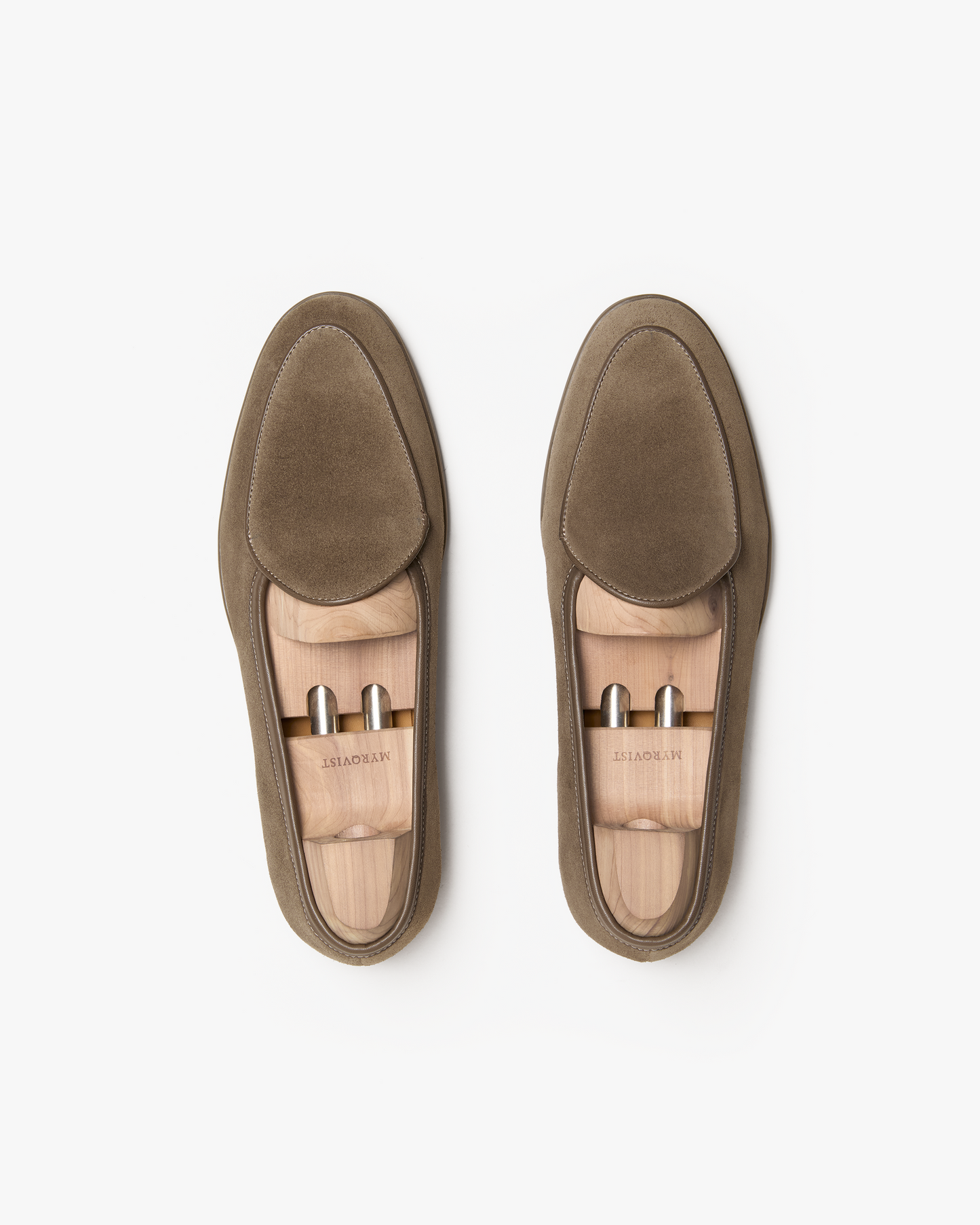 A pair of Ängby Walker in taupe suede displayed from above, showcasing the soft suede finish, clean minimalist lines, subtle piping, and wooden shoe trees inside each loafer.