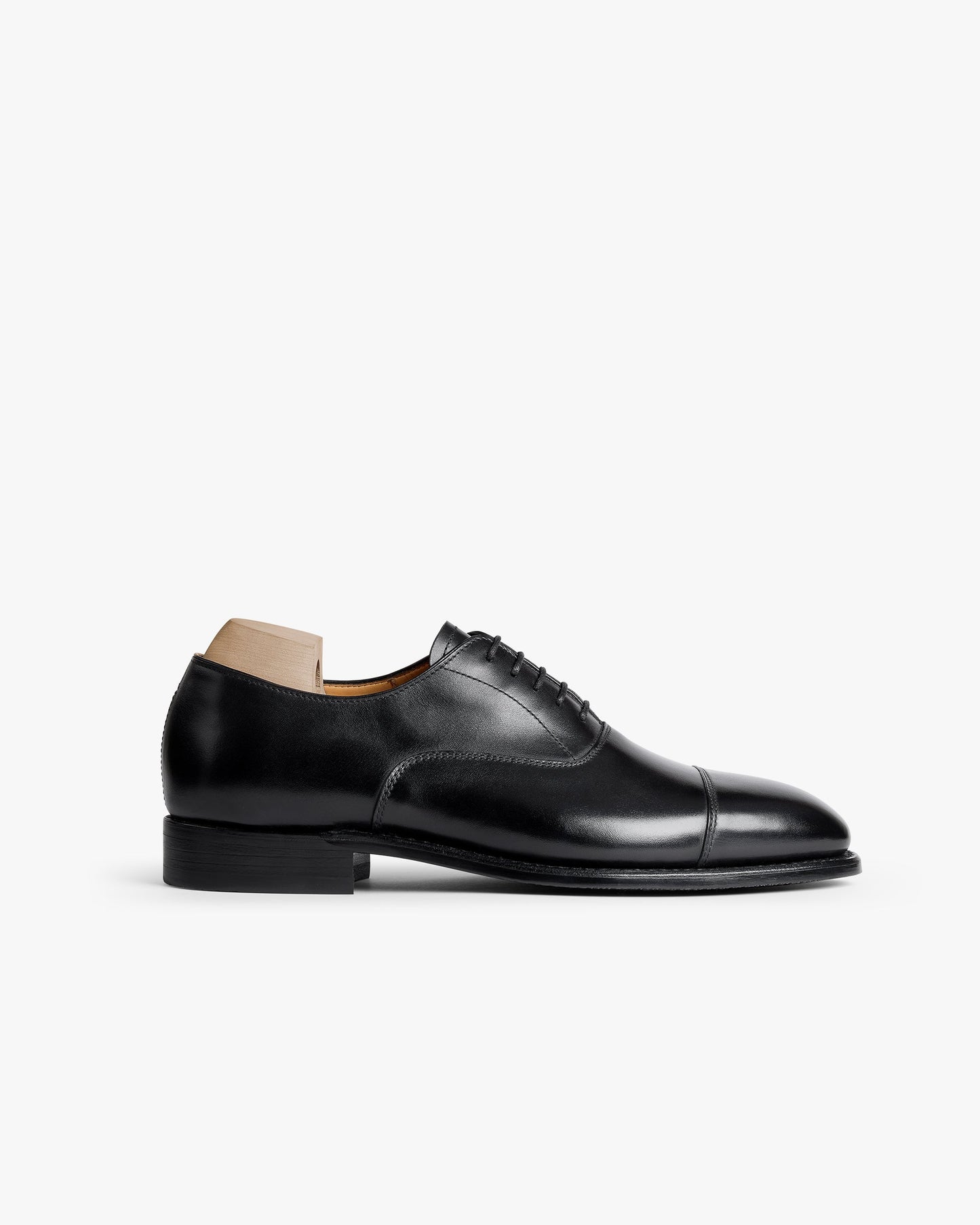 Äppelviken II in black calf features a classic cap-toe Oxford silhouette with closed lacing, polished full-grain leather, and a gently chiseled toe, presented with a wooden shoe tree for shape retention. The shoe’s refined lines and subtle sheen highlight its timeless design, ideal for pairing with formal suits or tailored trousers.