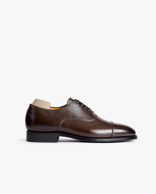 A single Äppelviken II Oxford shoe in dark brown calf leather is displayed in profile, featuring a polished cap toe, closed lacing, and subtle stitching details, set against a clean white background. The shoe’s elegant silhouette and refined finish highlight its suitability for formal occasions and business attire.