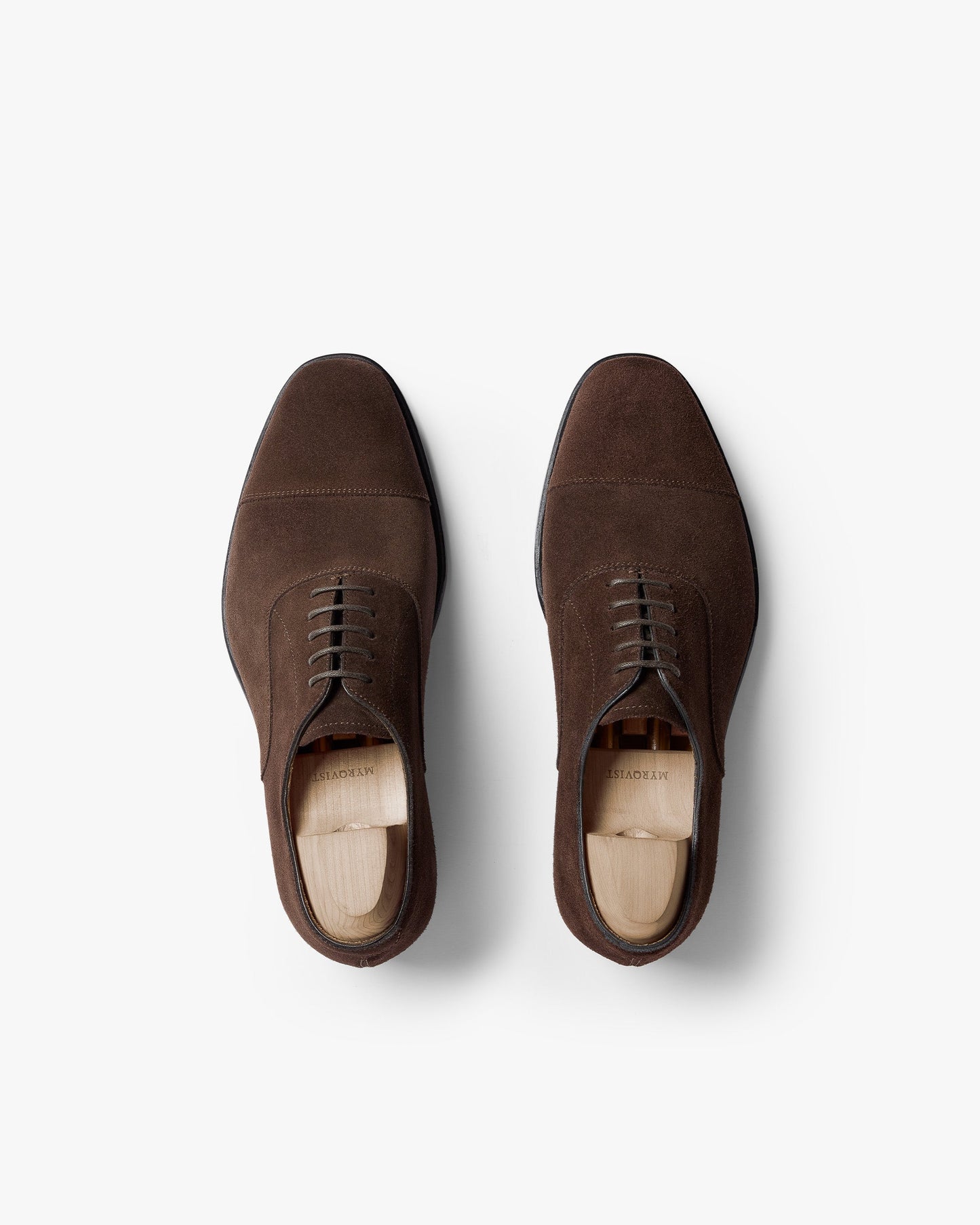 Pair of Äppelviken II in dark brown suede shown from above, highlighting the cap-toe oxford design, closed lacing, and soft suede texture with wooden shoe trees inside each shoe.