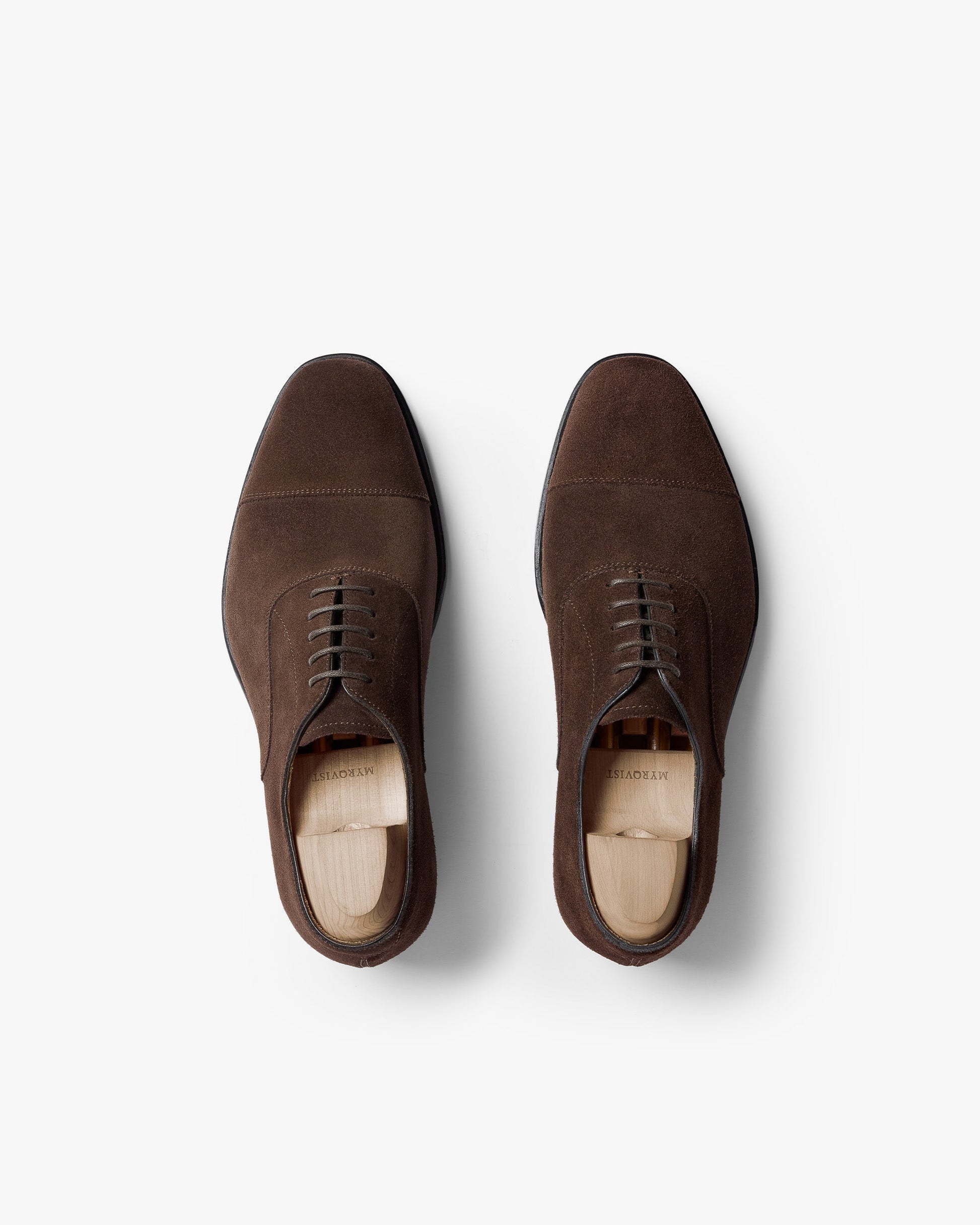 Pair of Äppelviken II in dark brown suede shown from above, highlighting the cap-toe oxford design, closed lacing, and soft suede texture with wooden shoe trees inside each shoe.