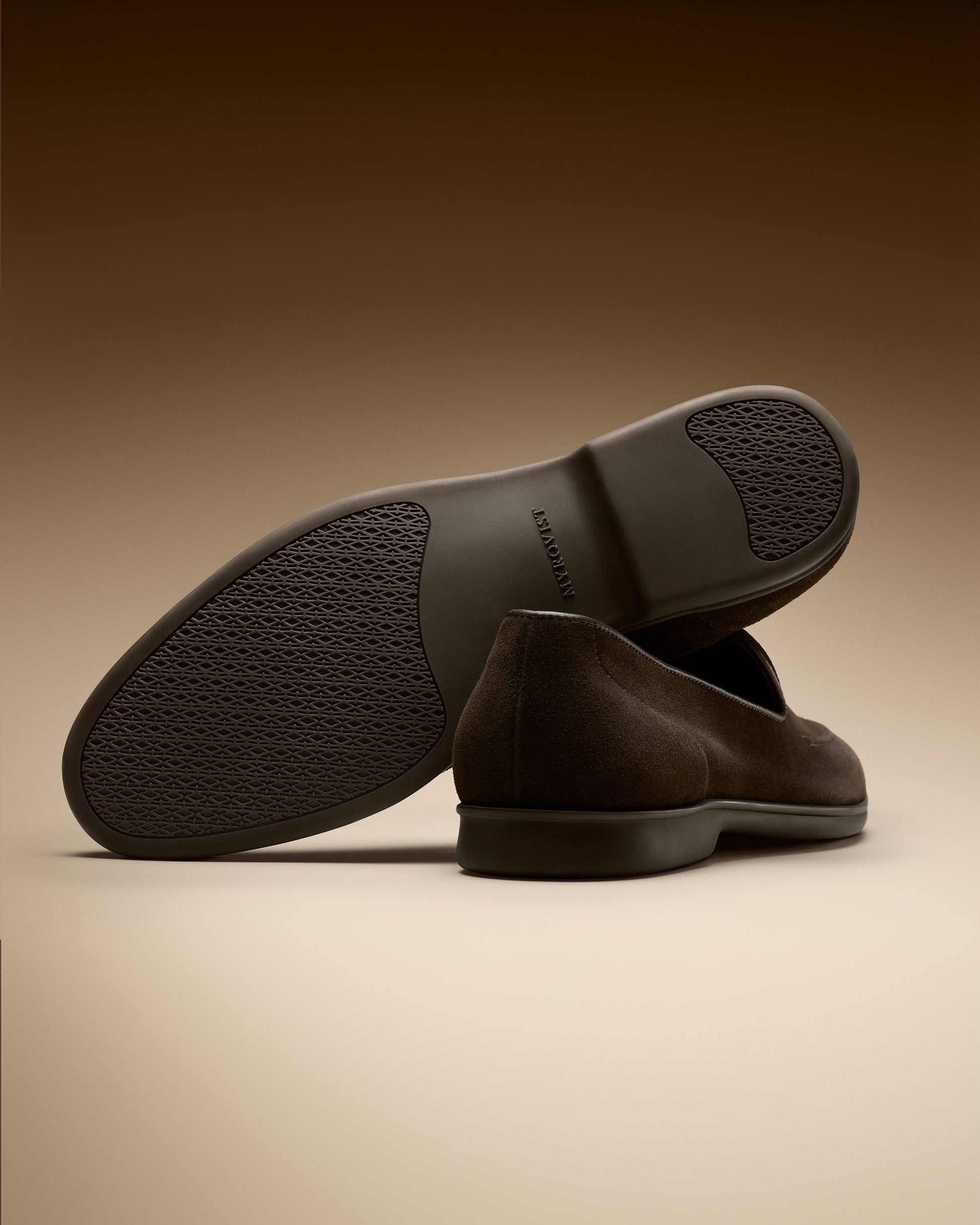 Brännö II in dark brown suede displayed on a warm gradient background, highlighting the textured rubber sole, clean stitching, and the refined suede finish of these men's loafers.