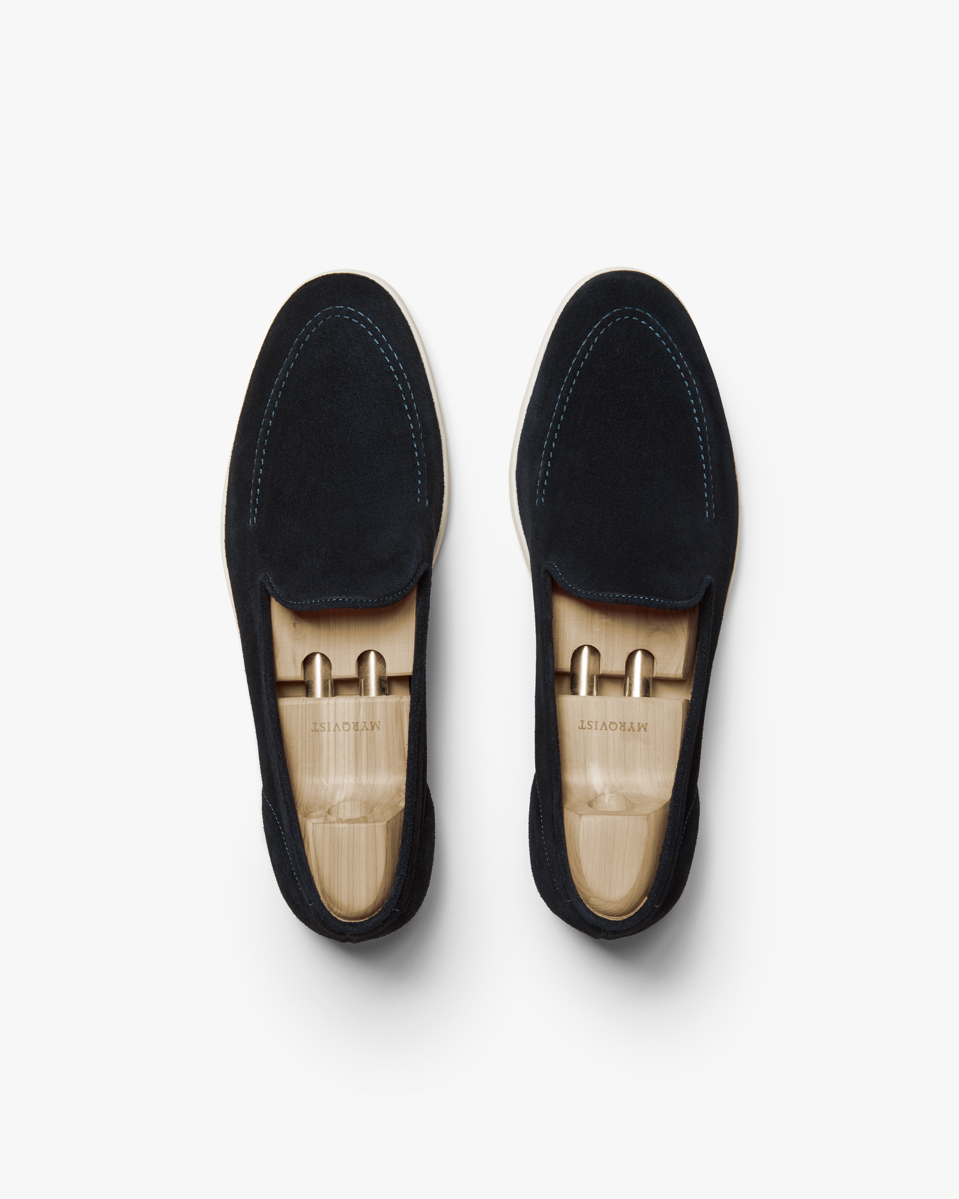 Brännö II in navy suede shown from above, highlighting the soft suede uppers, tonal stitching, and white rubber soles, each loafer fitted with a wooden shoe tree for shape retention.