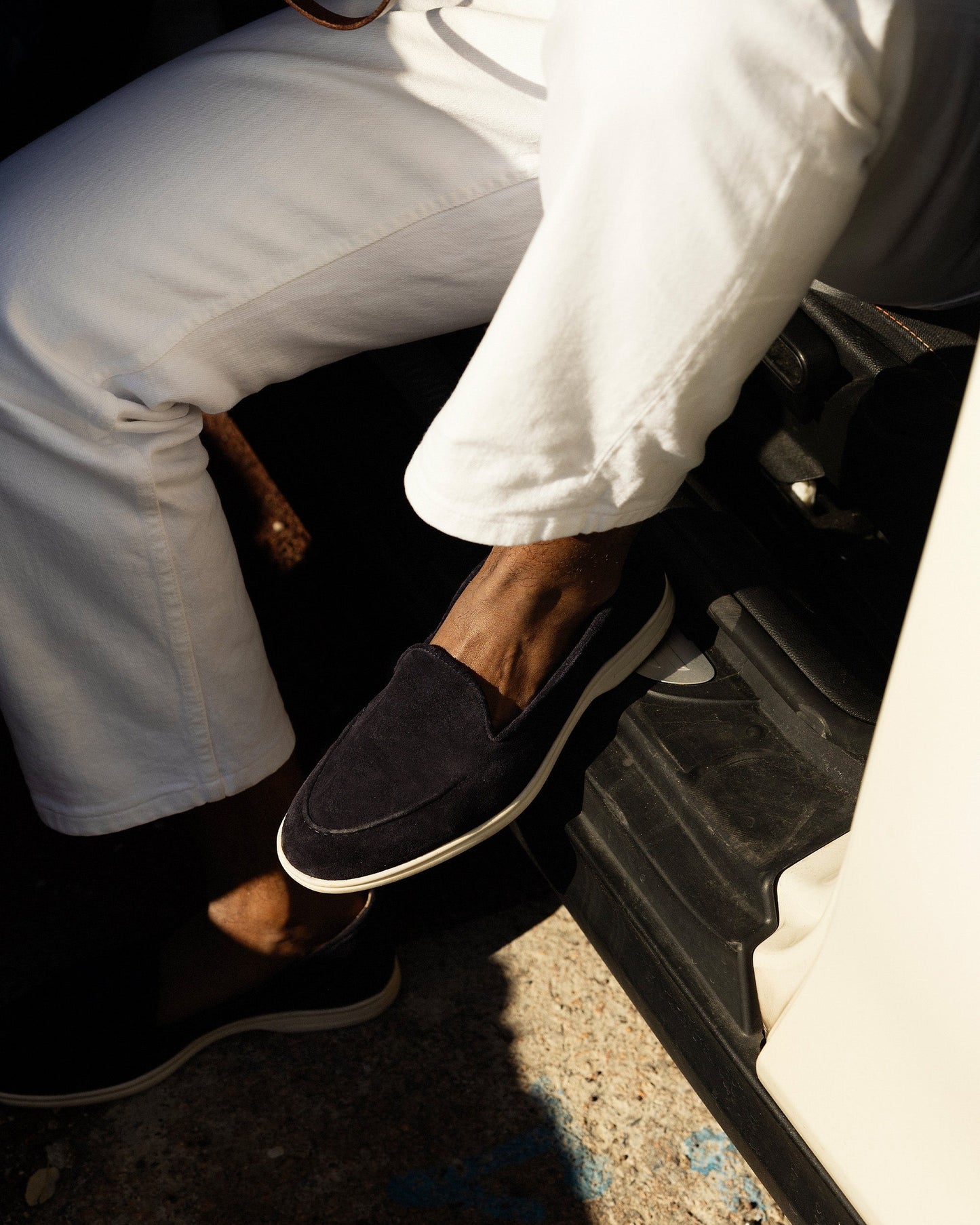 A man wears Brännö II in navy suede, styled with white denim, highlighting the loafer’s deep navy suede upper, tonal stitching, and white rubber sole in a relaxed, sunlit setting.