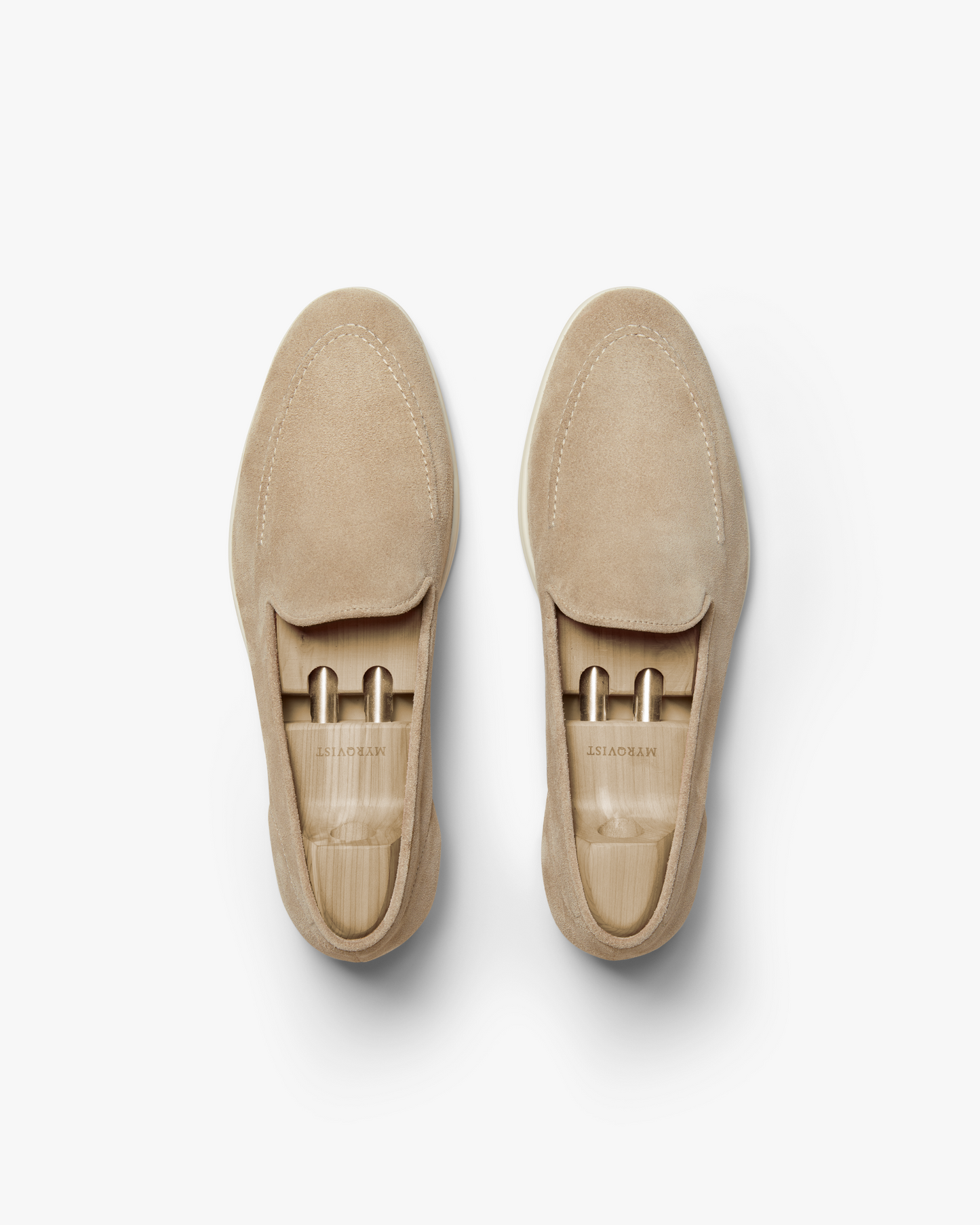 A pair of Brännö II in sand suede loafers shown from above, highlighting the soft beige suede upper, precise stitching, and wooden shoe trees inside each shoe for shape and care.