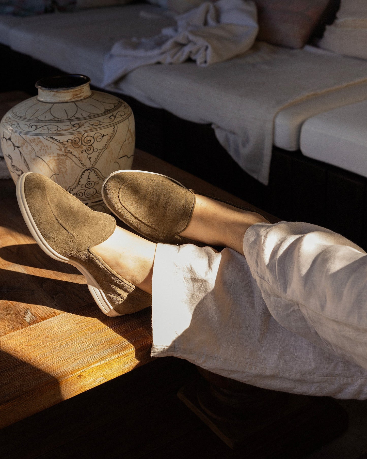 Brännö II in moss green suede styled with light linen trousers, shown in a relaxed indoor setting with natural sunlight highlighting the loafer's soft suede and white rubber sole.