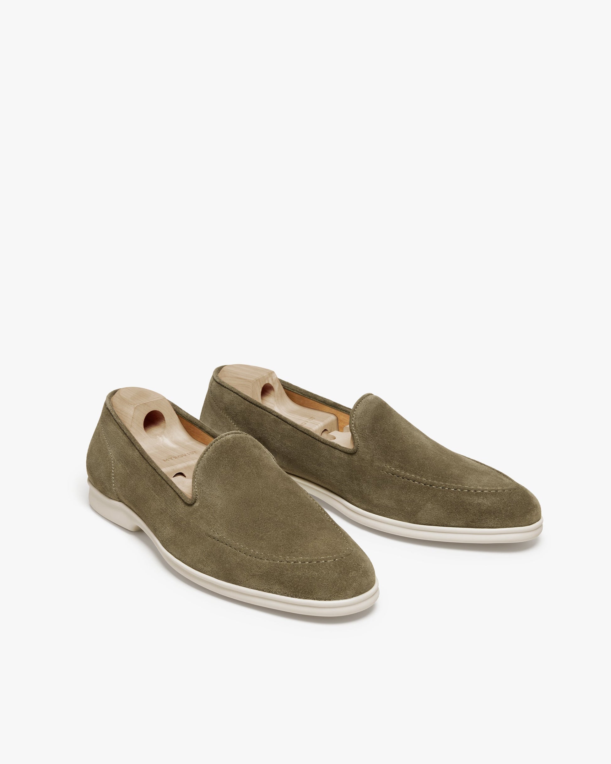 Brännö II in moss green suede displayed at an angle, featuring a minimalist loafer design with soft suede uppers, clean stitching, and contrasting white rubber soles, fitted with wooden shoe trees to preserve their shape.