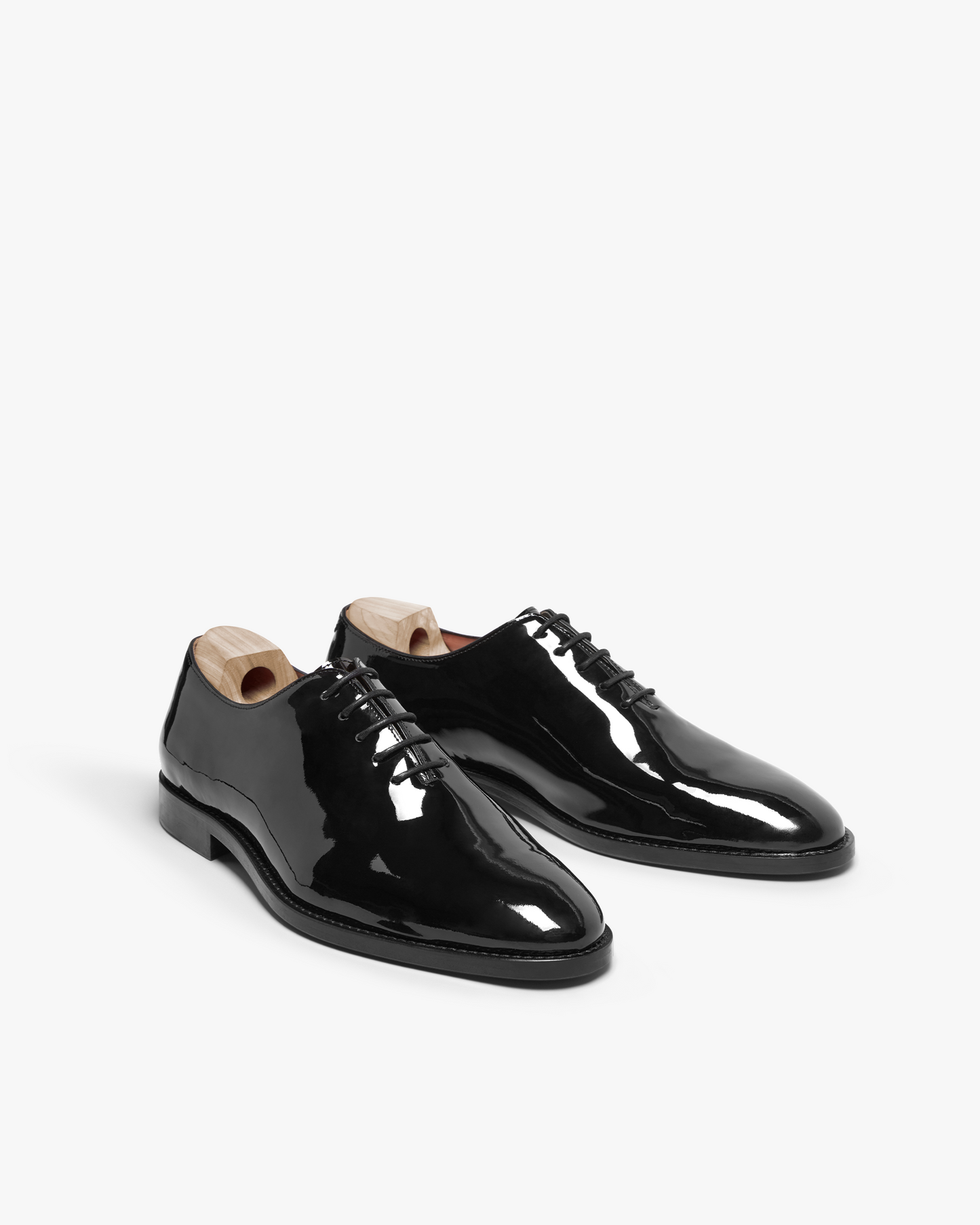 Drottningholm in black patent leather displayed at an angle, showcasing the whole-cut Oxford silhouette, high-gloss finish, almond-shaped toes, and wooden shoe trees, ideal for pairing with formal suits or tuxedos.