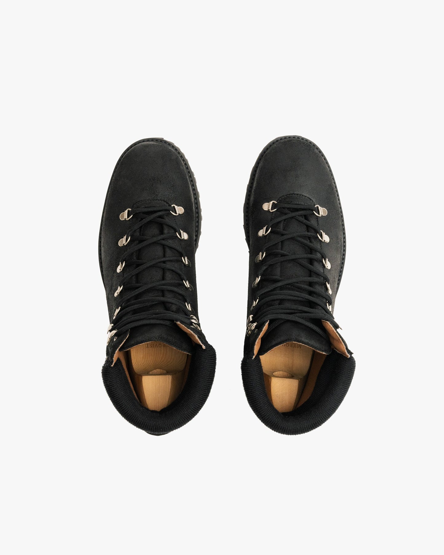 Duved in black waxed suede shown from above, featuring water-repellent suede uppers, metal eyelets, padded collars, and sturdy hiking soles, with wooden shoe trees inside each boot.