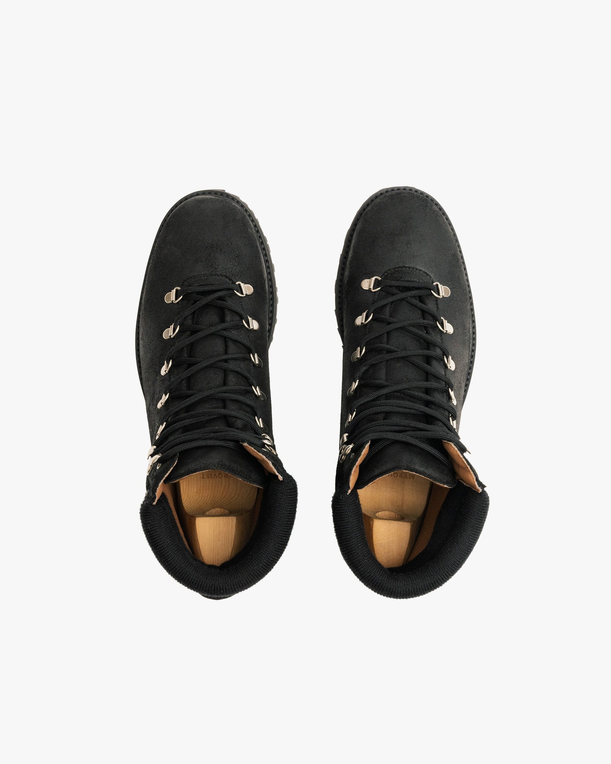 Duved in black waxed suede shown from above, featuring water-repellent suede uppers, metal eyelets, padded collars, and sturdy hiking soles, with wooden shoe trees inside each boot.