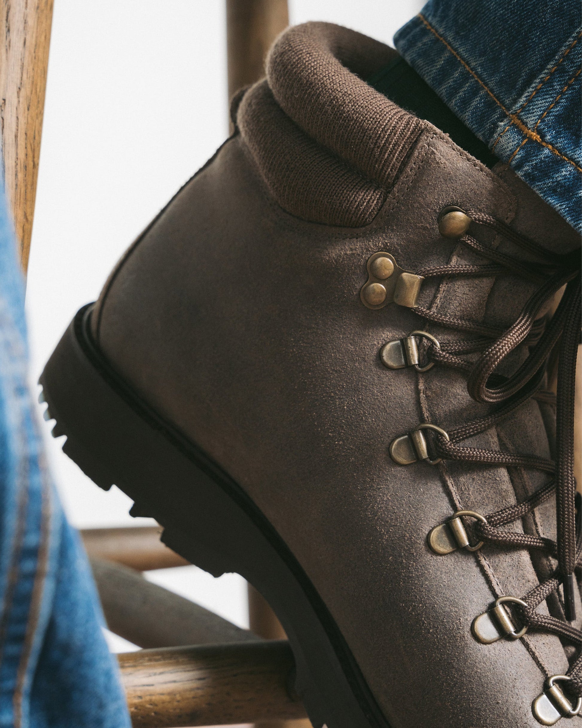 Close-up of Duved in taupe waxed suede, highlighting the textured suede upper, brass-finished hardware, and padded collar, styled with denim for a relaxed, versatile look.