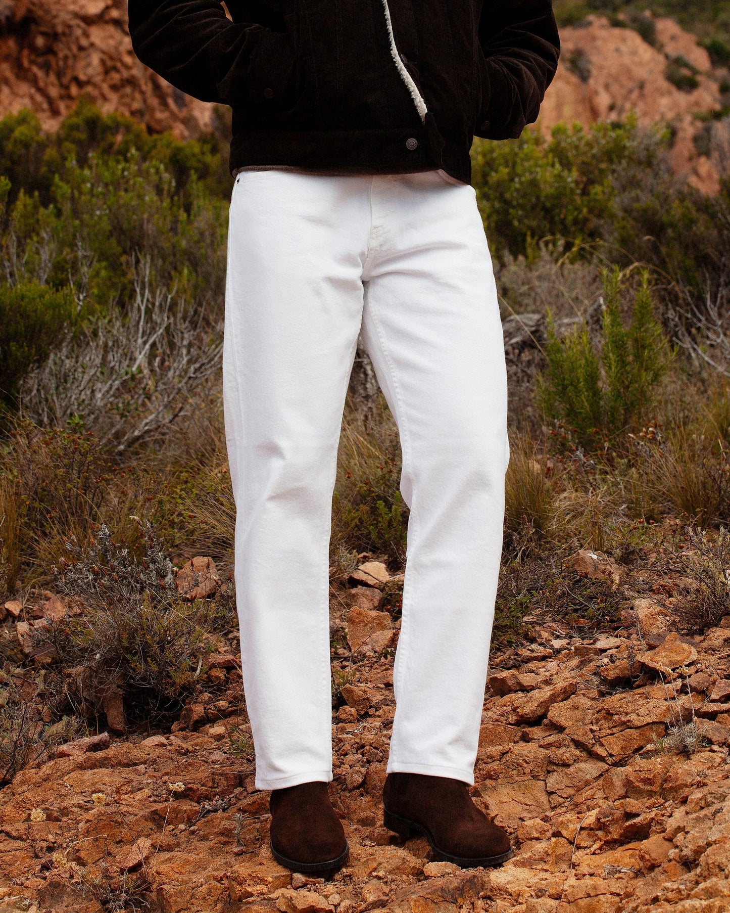 Elfvik Chelsea boots in dark brown suede are styled outdoors with white trousers and a dark jacket, highlighting their water-repellent suede and versatile design for both rugged and refined settings.
