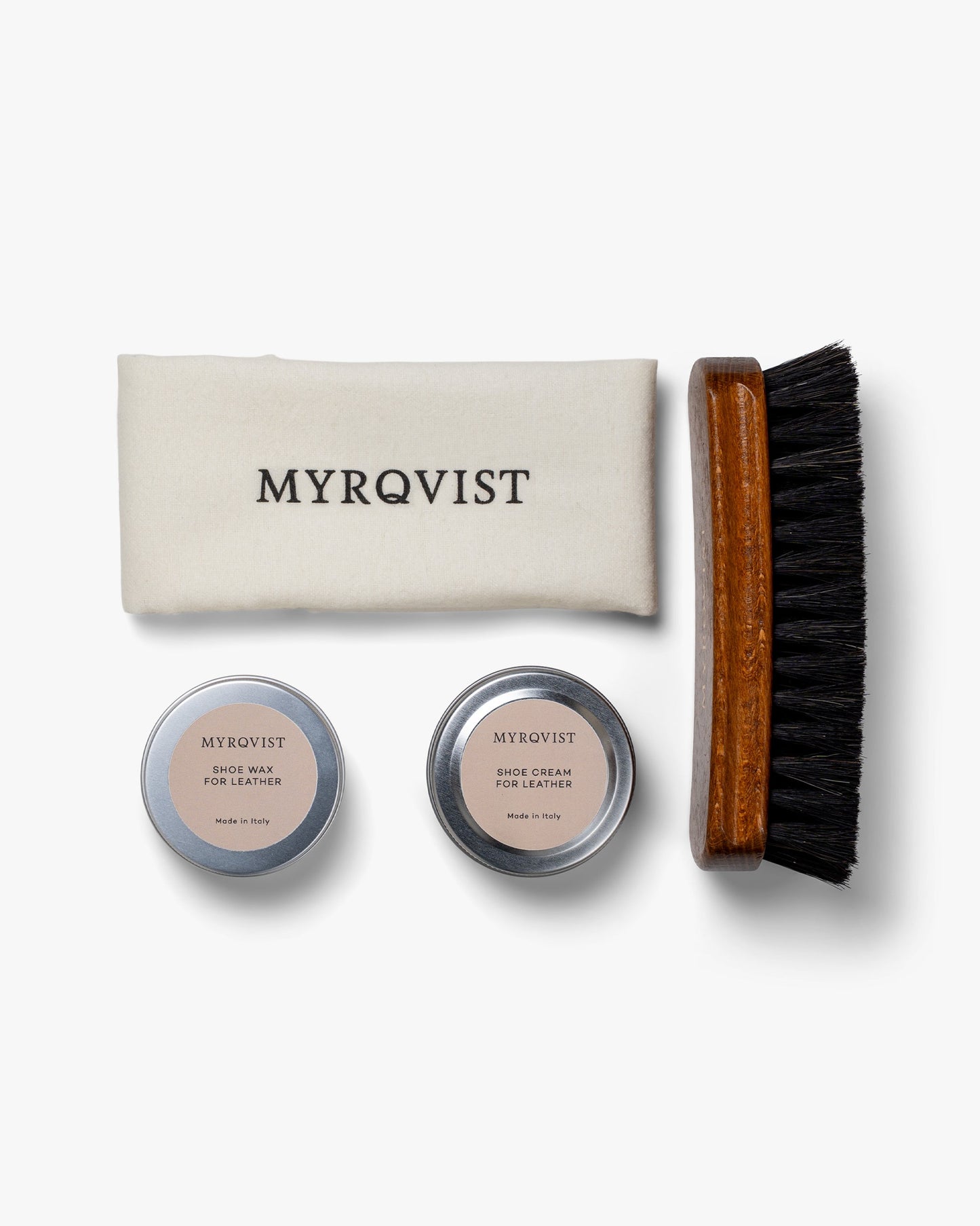 Shoe Care Kit – Leather arranged on a white background, featuring a soft Myrqvist-branded polishing cloth, a wooden-handled brush with dark bristles, and minimalist tins of shoe cream and wax for leather shoe maintenance.