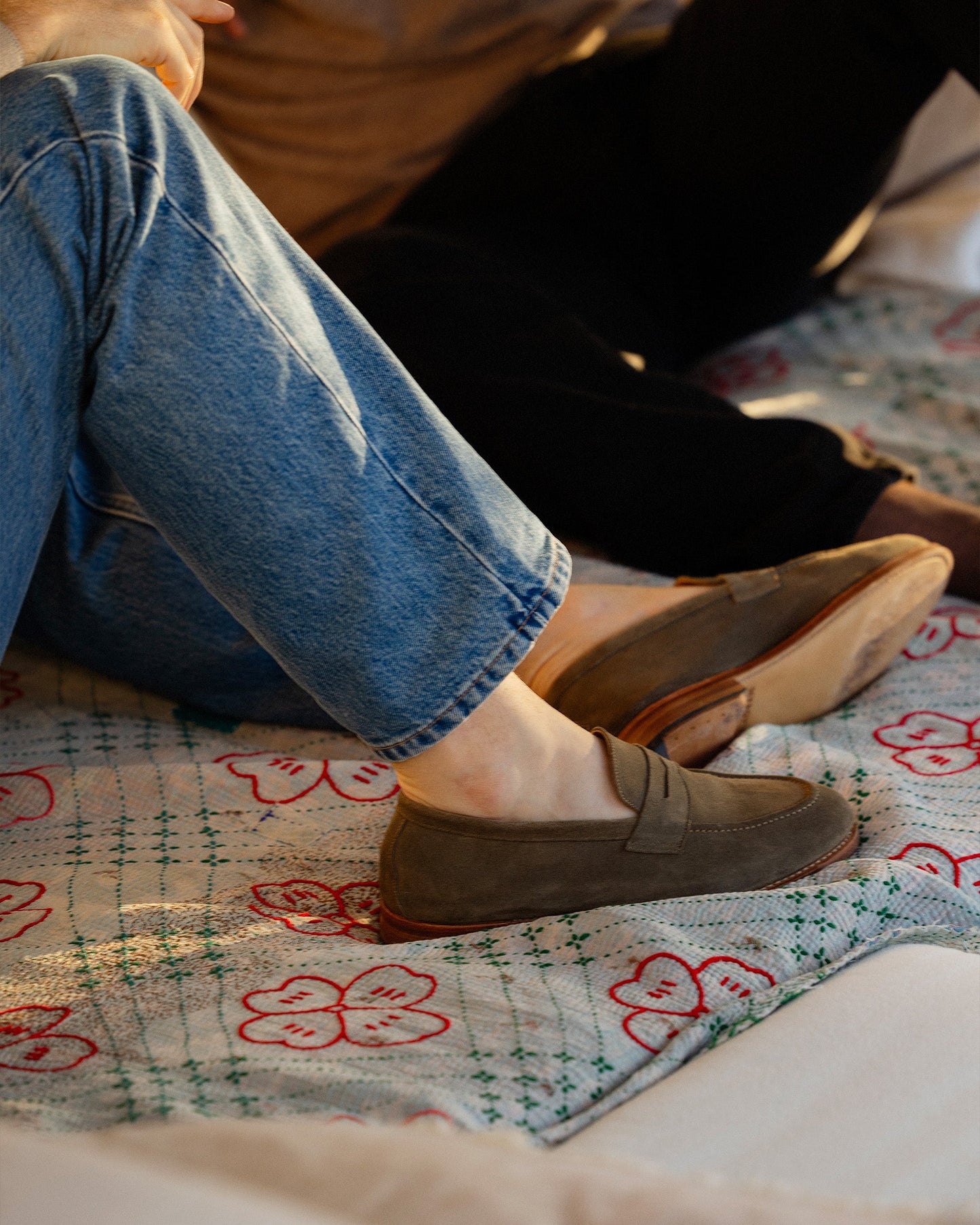 A man wears Lysekil II in green suede, styled with relaxed denim jeans while seated on a patterned blanket, highlighting the loafer’s soft suede texture and versatile, casual elegance.
