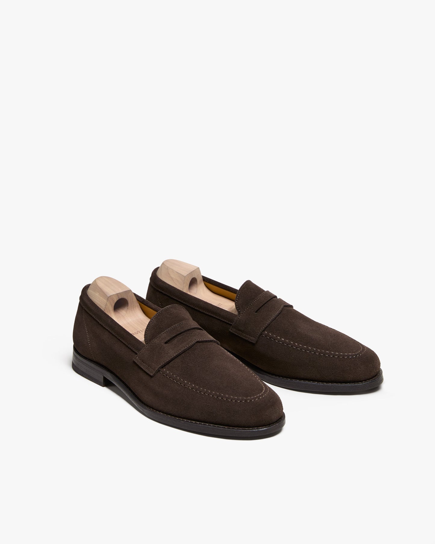Lysekil II in dark brown suede displayed at a three-quarter angle, featuring a classic penny loafer design with apron stitching, rounded toe, and wooden shoe trees to maintain shape. The rich suede finish and clean lines highlight its refined, versatile style for both business casual and relaxed outfits.