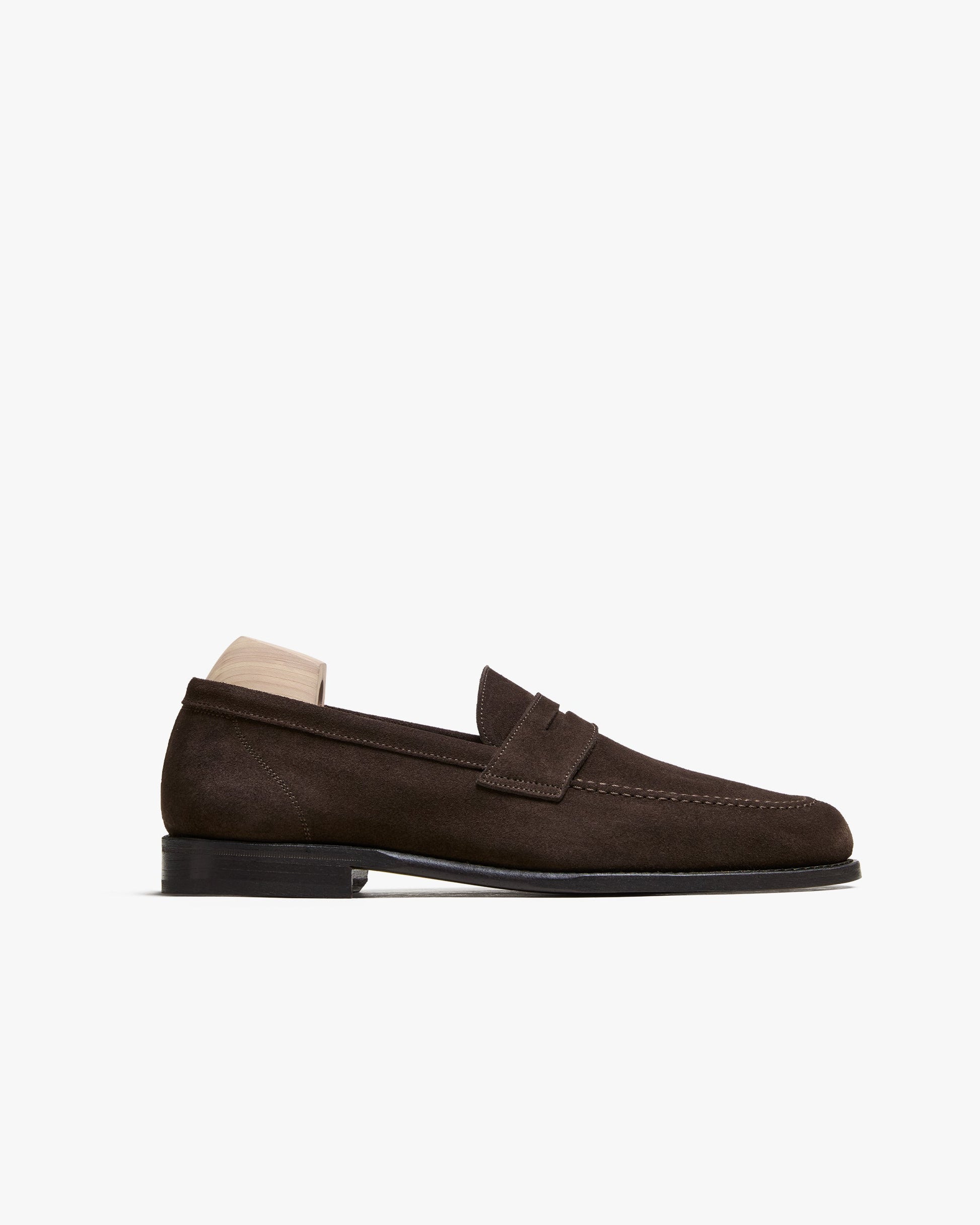 Lysekil II in dark brown suede features a classic penny loafer silhouette with an apron front, rounded toe, and subtle stitching, shown with a wooden shoe tree for shape. The rich suede and clean lines highlight its refined, versatile style, ideal for pairing with slacks or denim.