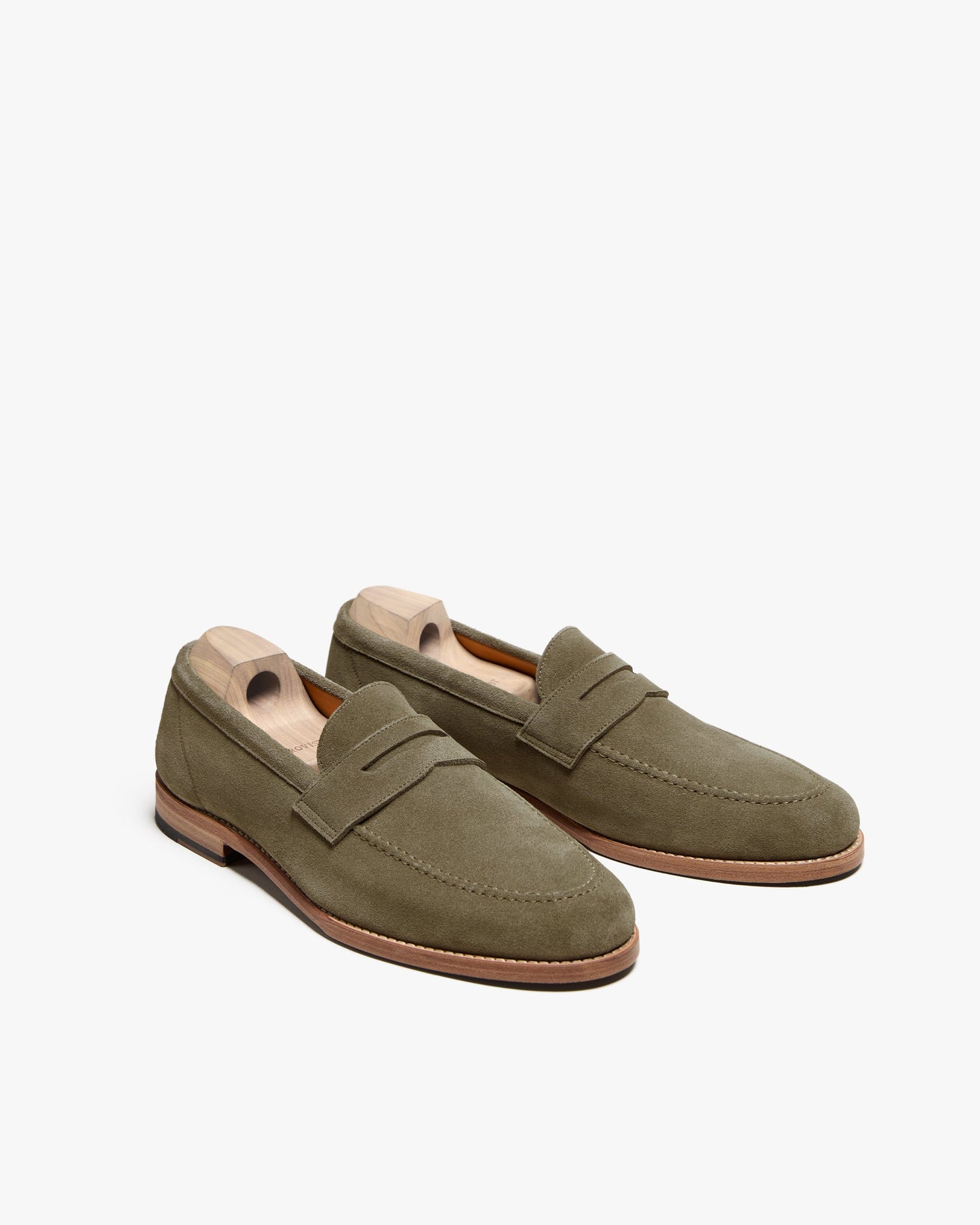 Lysekil II in green suede features a pair of men's penny loafers with a softly rounded toe, apron front, and subtle stitching, shown with wooden shoe trees to maintain their elegant shape.