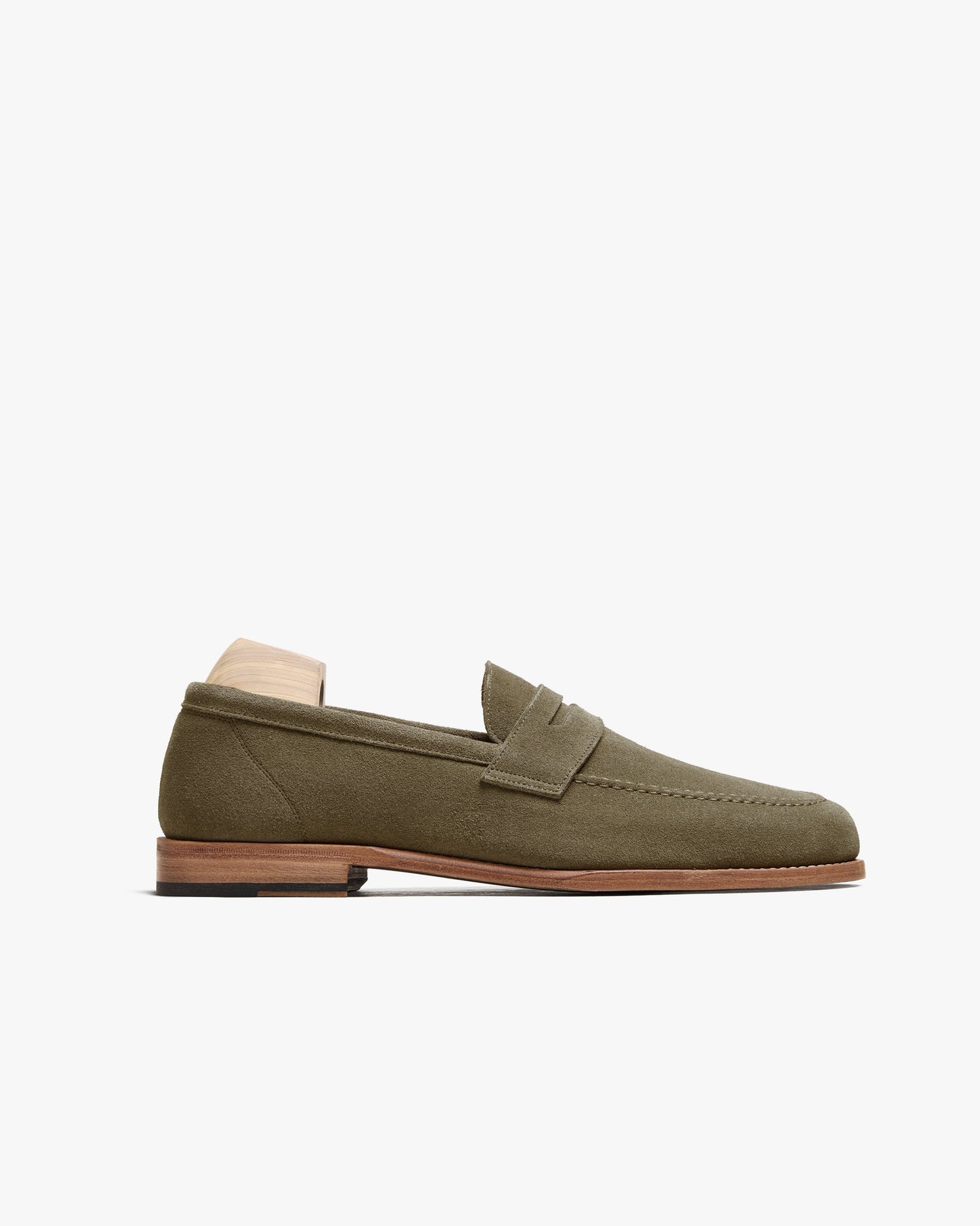 Lysekil II in green suede features a classic penny loafer silhouette with a softly rounded toe, apron front, and subtle stitching, set on a leather sole with a wooden shoe tree inside. The olive green suede offers a refined, versatile look ideal for pairing with tailored slacks or casual trousers.