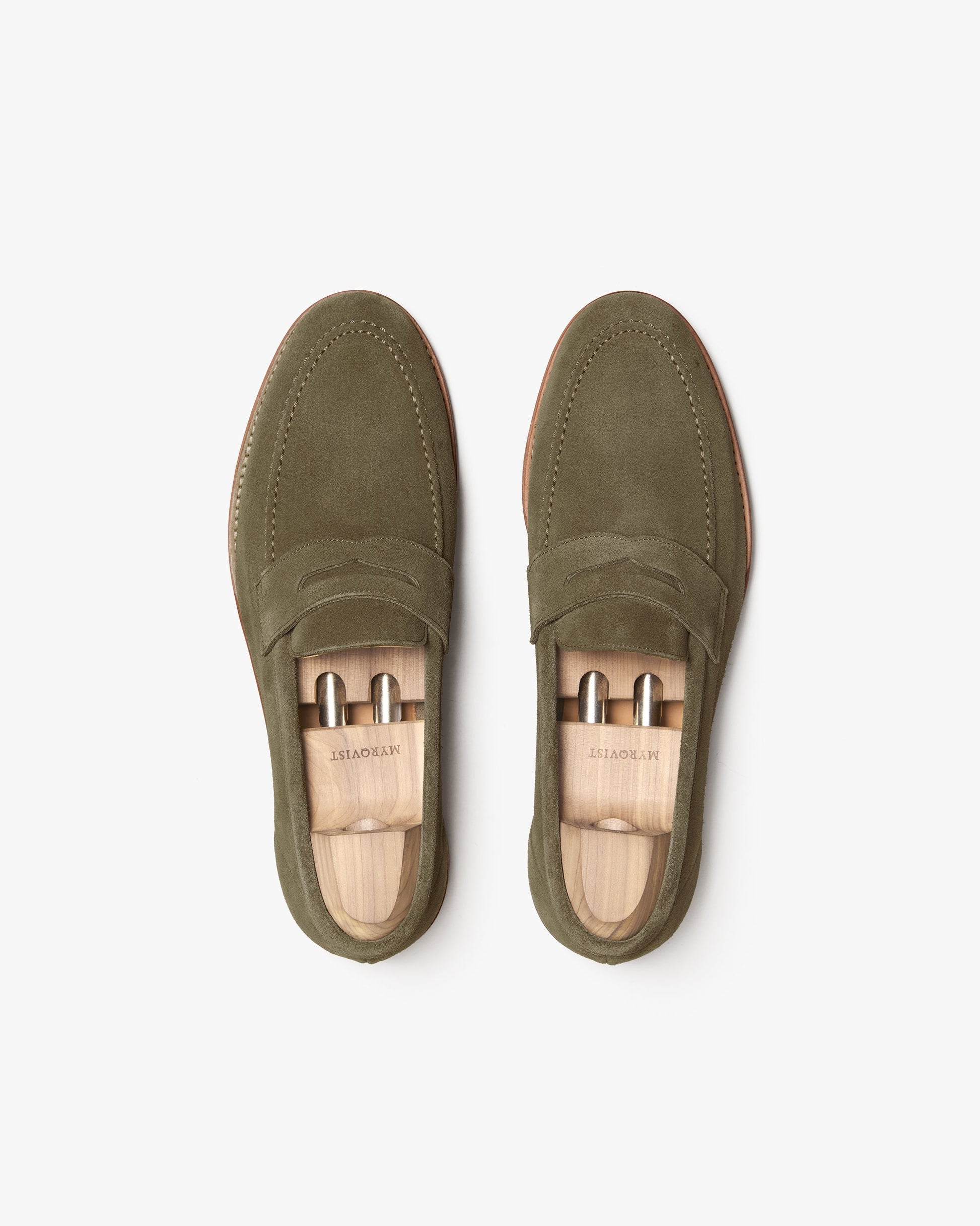 A pair of Lysekil II in green suede shown from above, highlighting the soft suede texture, penny strap detail, and wooden shoe trees inside each loafer for shape and care.