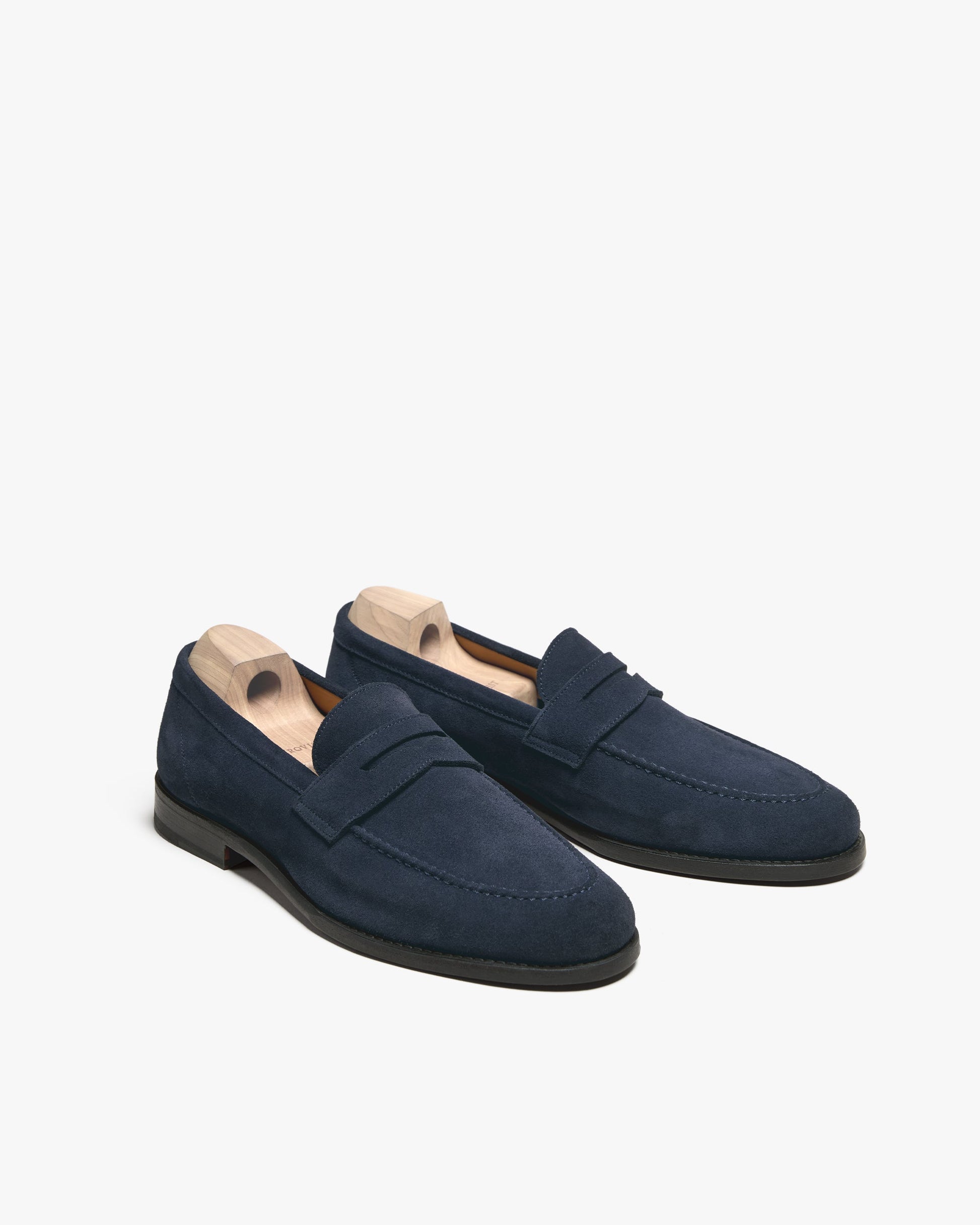 Lysekil II in navy suede displayed at an angle, featuring deep blue suede uppers, classic penny straps, apron toe stitching, and wooden shoe trees inside each loafer.
