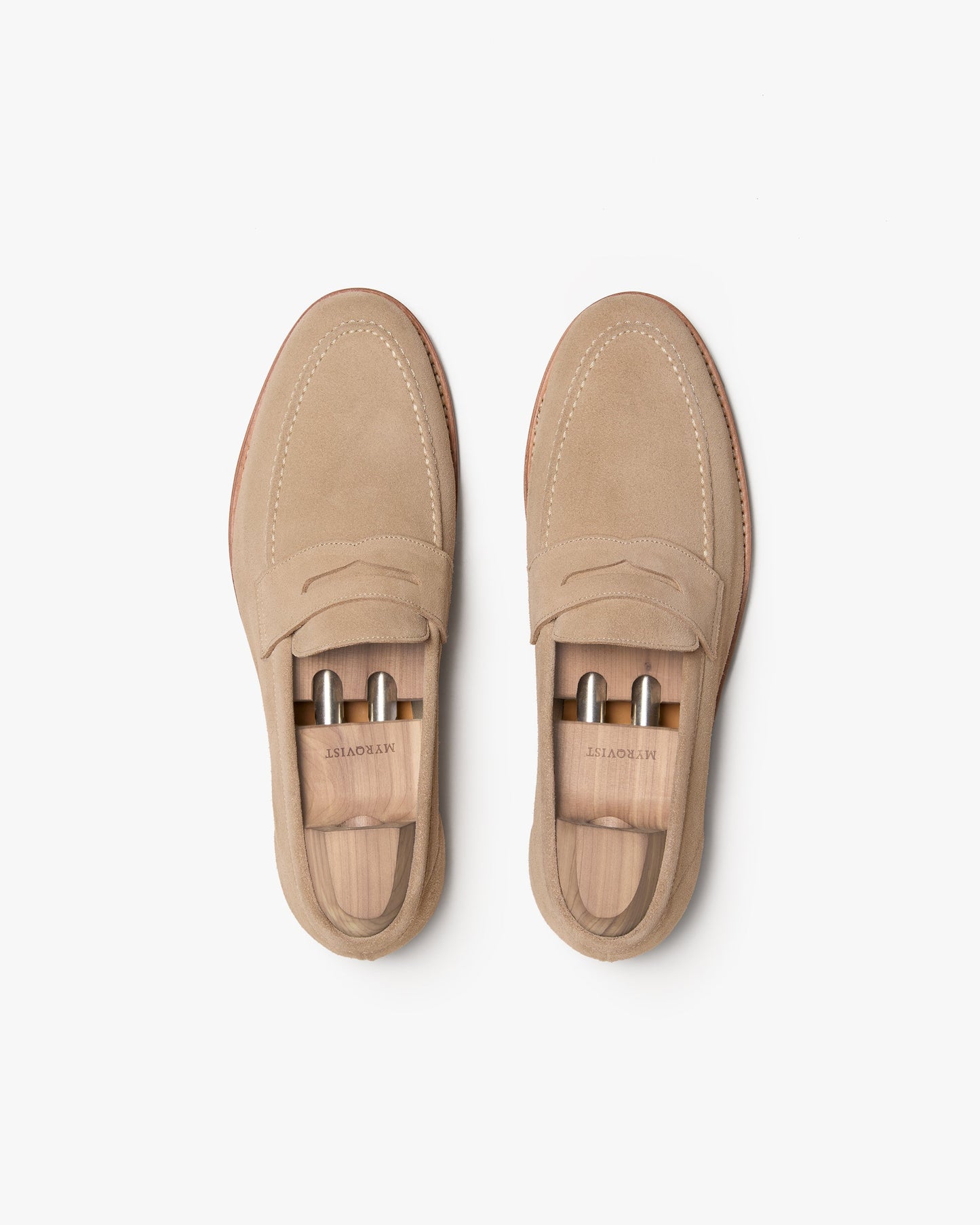 A pair of Lysekil II in sand suede penny loafers shown from above, highlighting the soft suede finish, classic apron stitching, and wooden shoe trees inside for shape retention.