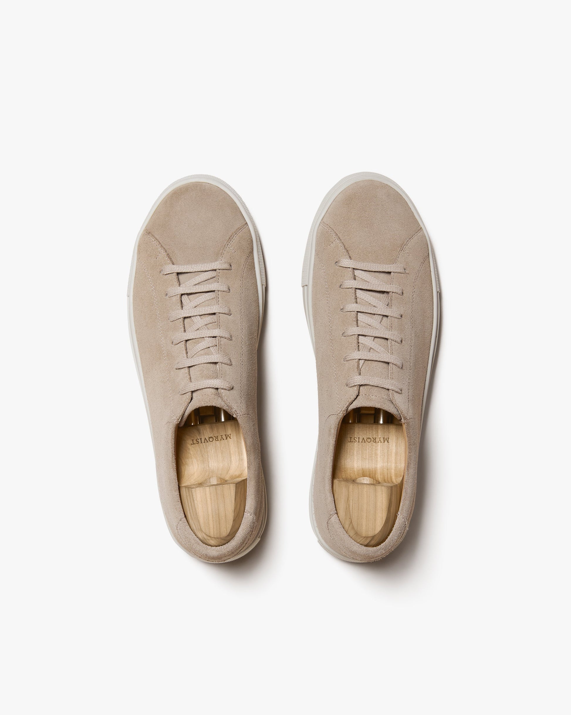 Oaxen in sand suede shown from above, displaying the soft beige suede uppers, tonal laces, and clean off-white soles, with wooden shoe trees inside each sneaker for structure.
