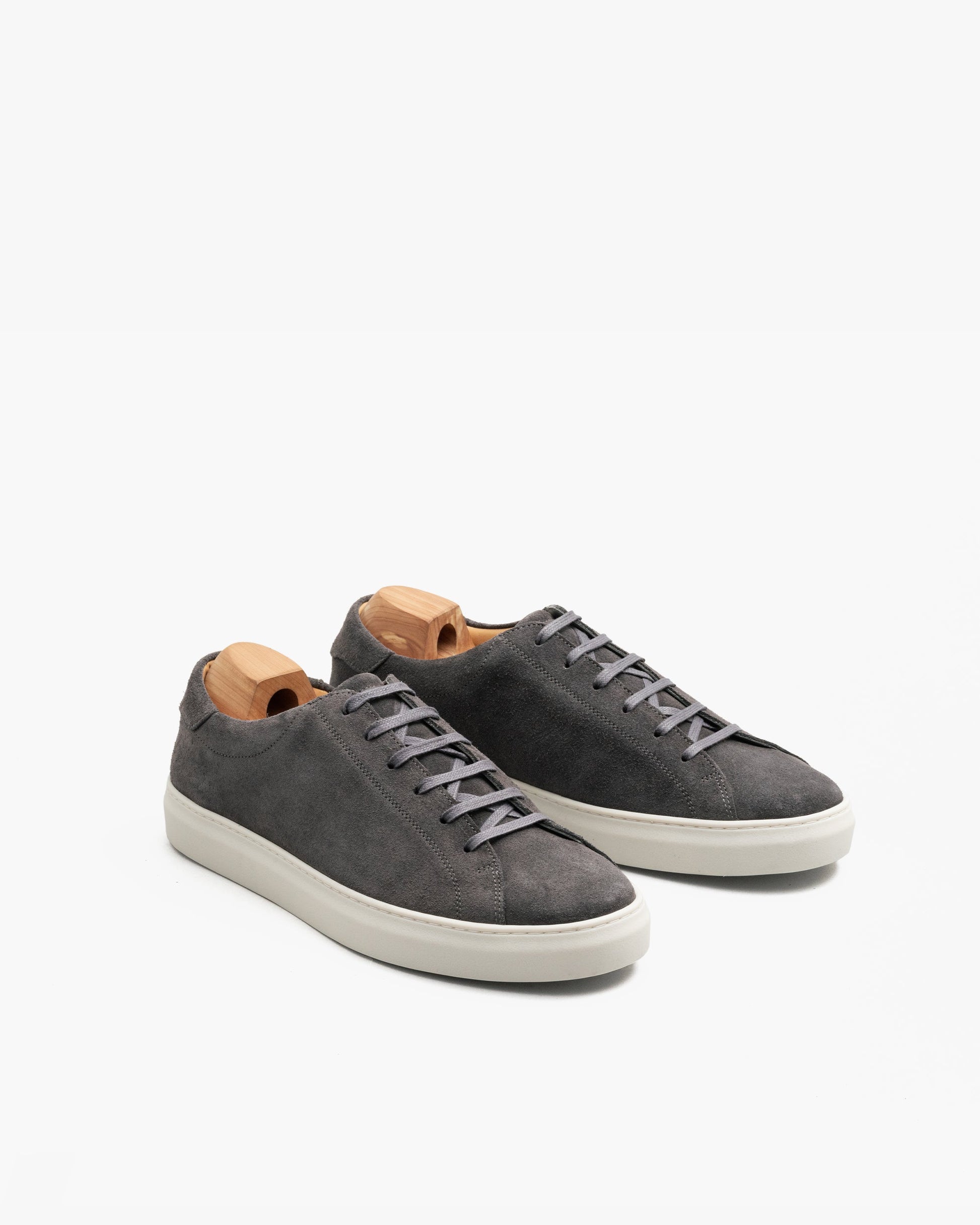 Oaxen sneakers in dark grey suede with flat tonal laces, seamless stitching, and off-white soles, displayed at an angle with wooden shoe trees inside each shoe.