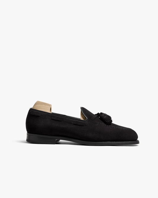 Mölle II in black suede features an apron fronted tassel loafer design with a matte finish, almond-shaped toe, and subtle stitching, shown with a wooden shoe tree inserted.