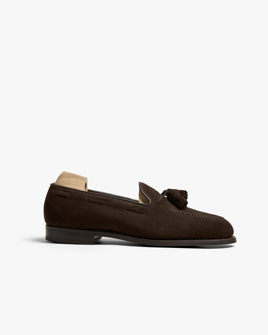 Mölle II in dark brown suede features an apron front, tassel detailing, and an almond-shaped toe, shown in a side profile against a white background with a wooden shoe tree inserted.