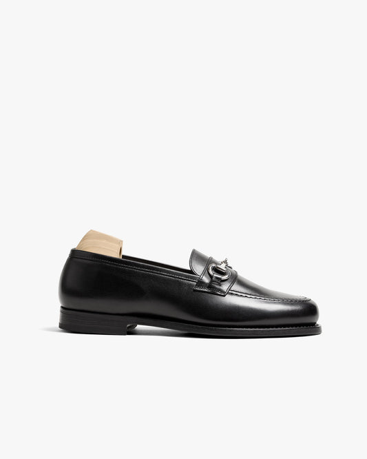 Karlberg loafer in black calf leather with a rounded toe, silver-toned horsebit detail, and a sleek rubber sole, displayed with a wooden shoe tree.