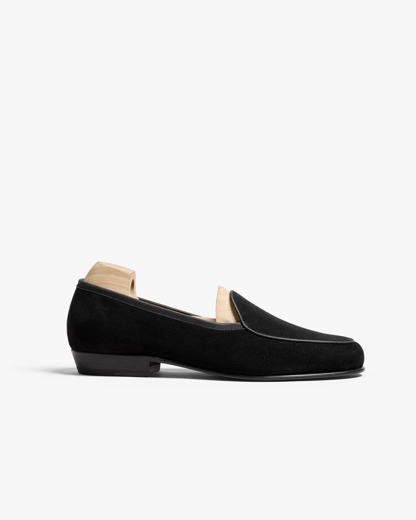 Ängby in black suede features a classic Belgian loafer silhouette with a velvety suede finish, refined piping, and a low stacked heel, shown with a wooden shoe tree for shape.