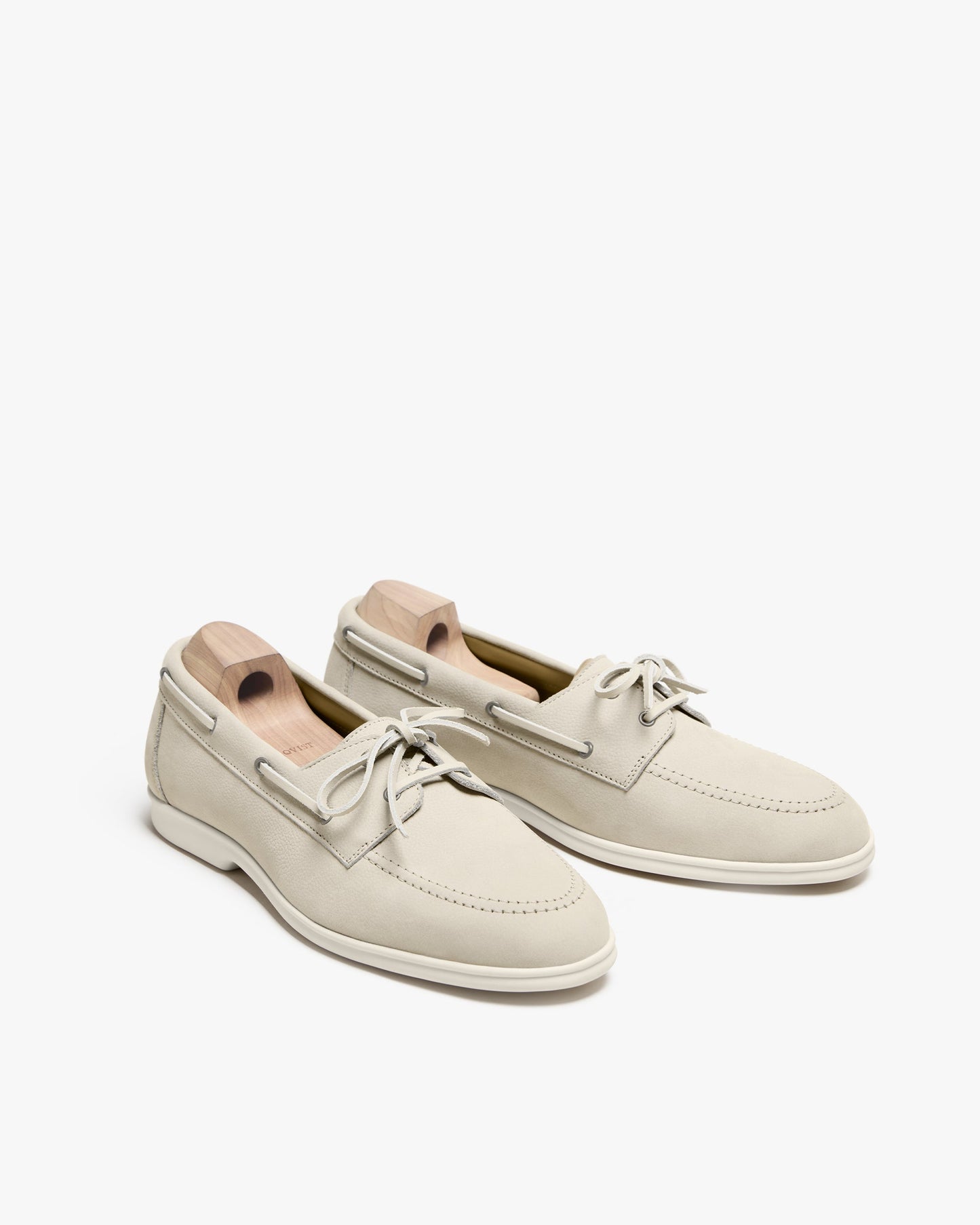 Sandhamn in beige nubuck displayed at an angle, showcasing the soft nubuck upper, hand-stitched detailing, minimalist lacing, and pale sole, with wooden shoe trees inside to maintain the shoes' shape.